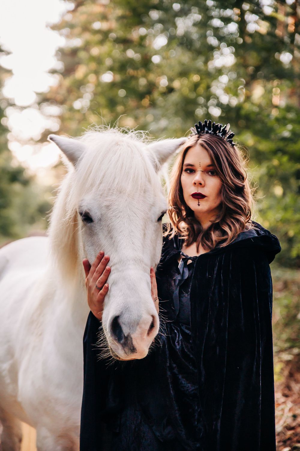 Ethereal portrait of white horse and cloaked figure in autumn forest setting.