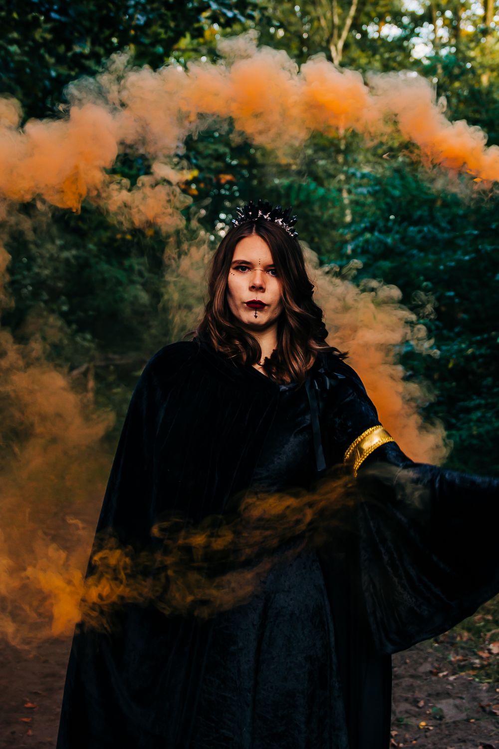 Dramatic portrait with flowing orange smoke effects in a dark forest setting.