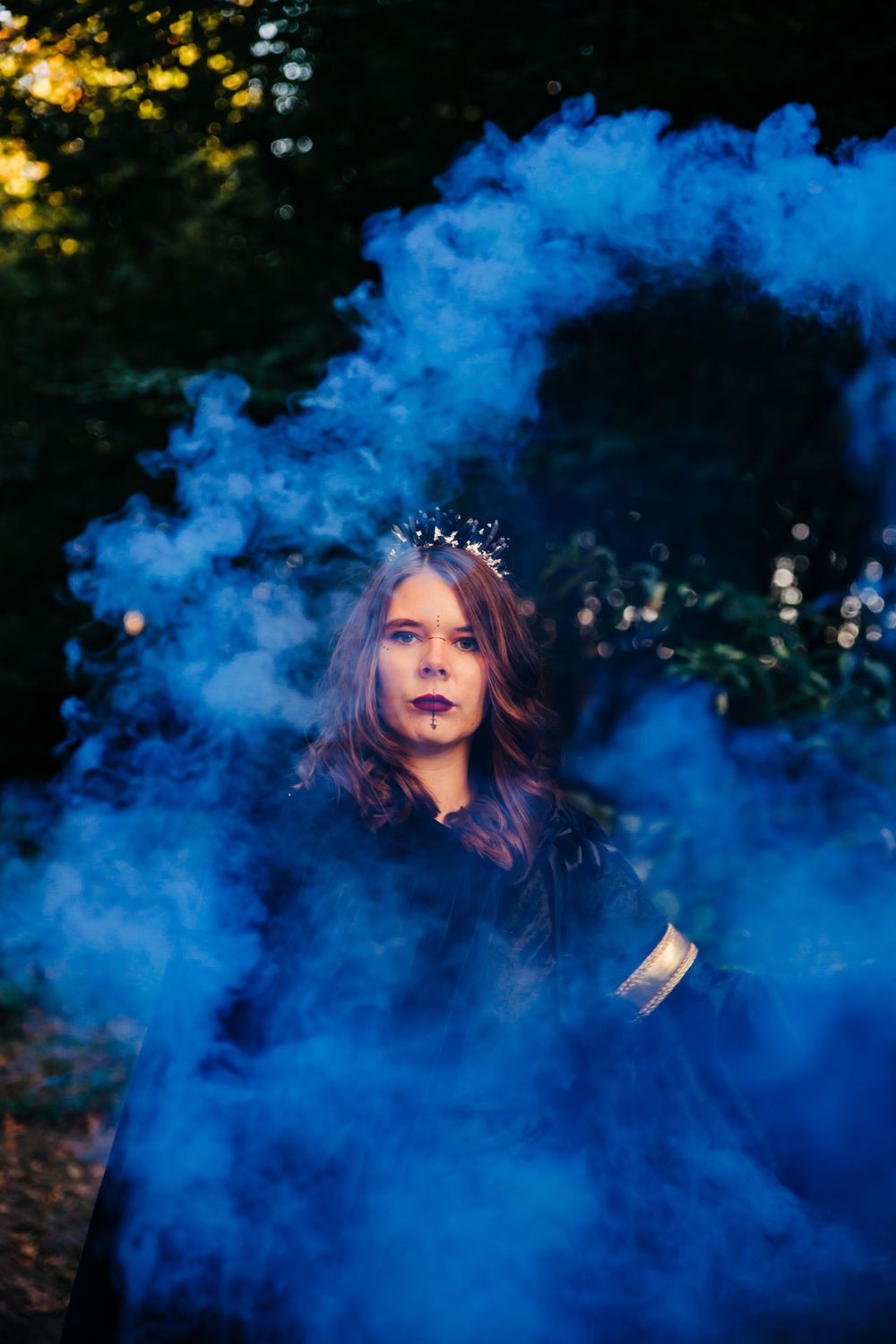 Royal gothic aesthetic captured with blue smoke effects in forest setting.