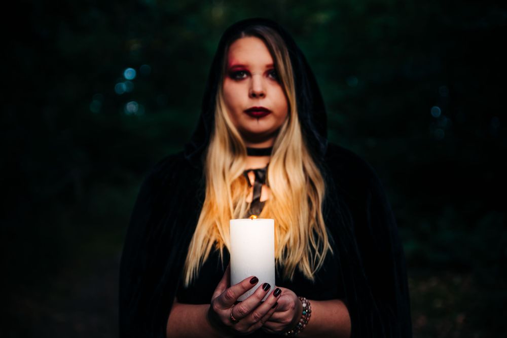 Atmospheric portrait holding white candle in dark forest setting.