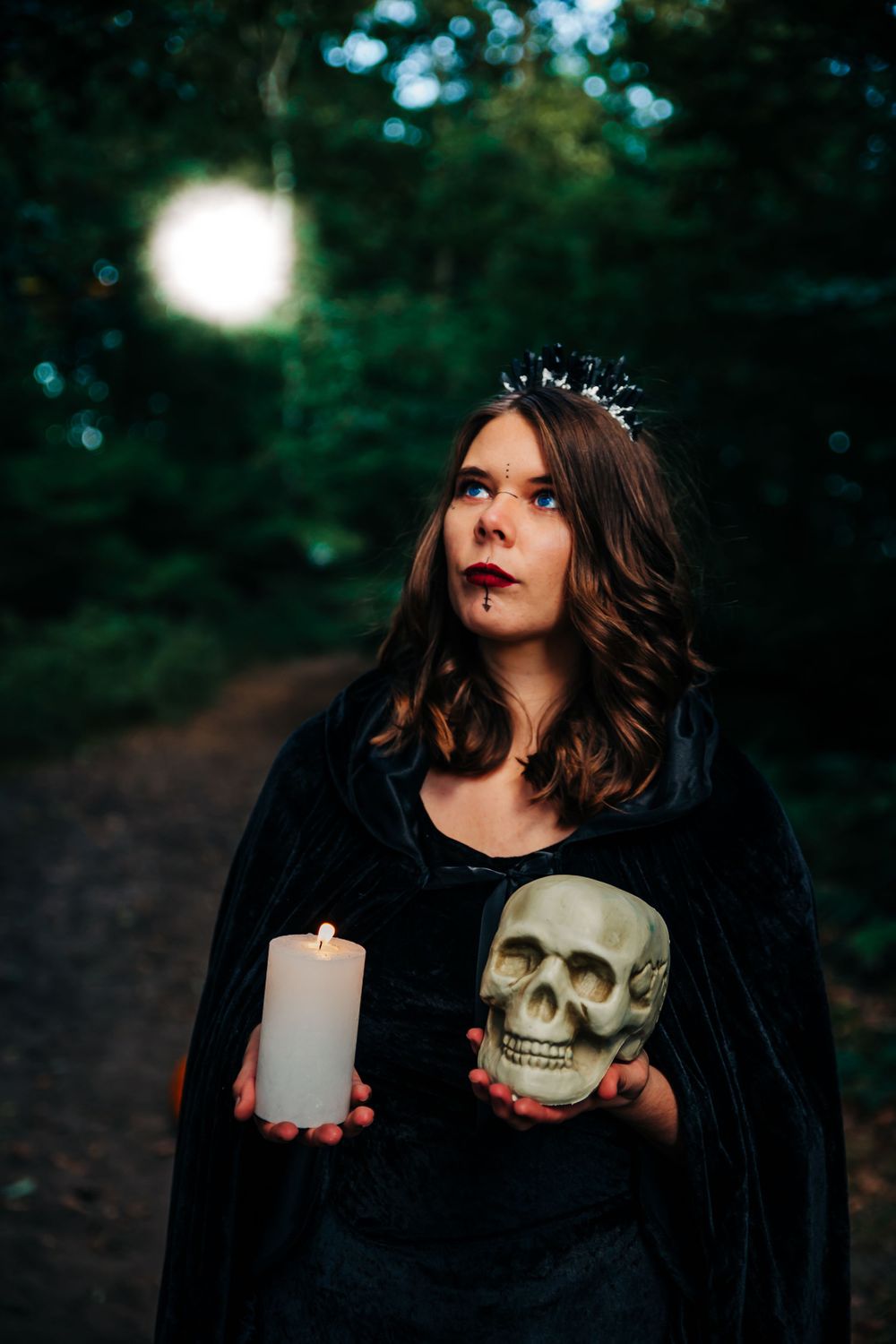 Dark atmospheric portrait with skull prop and white candle in moody forest setting.