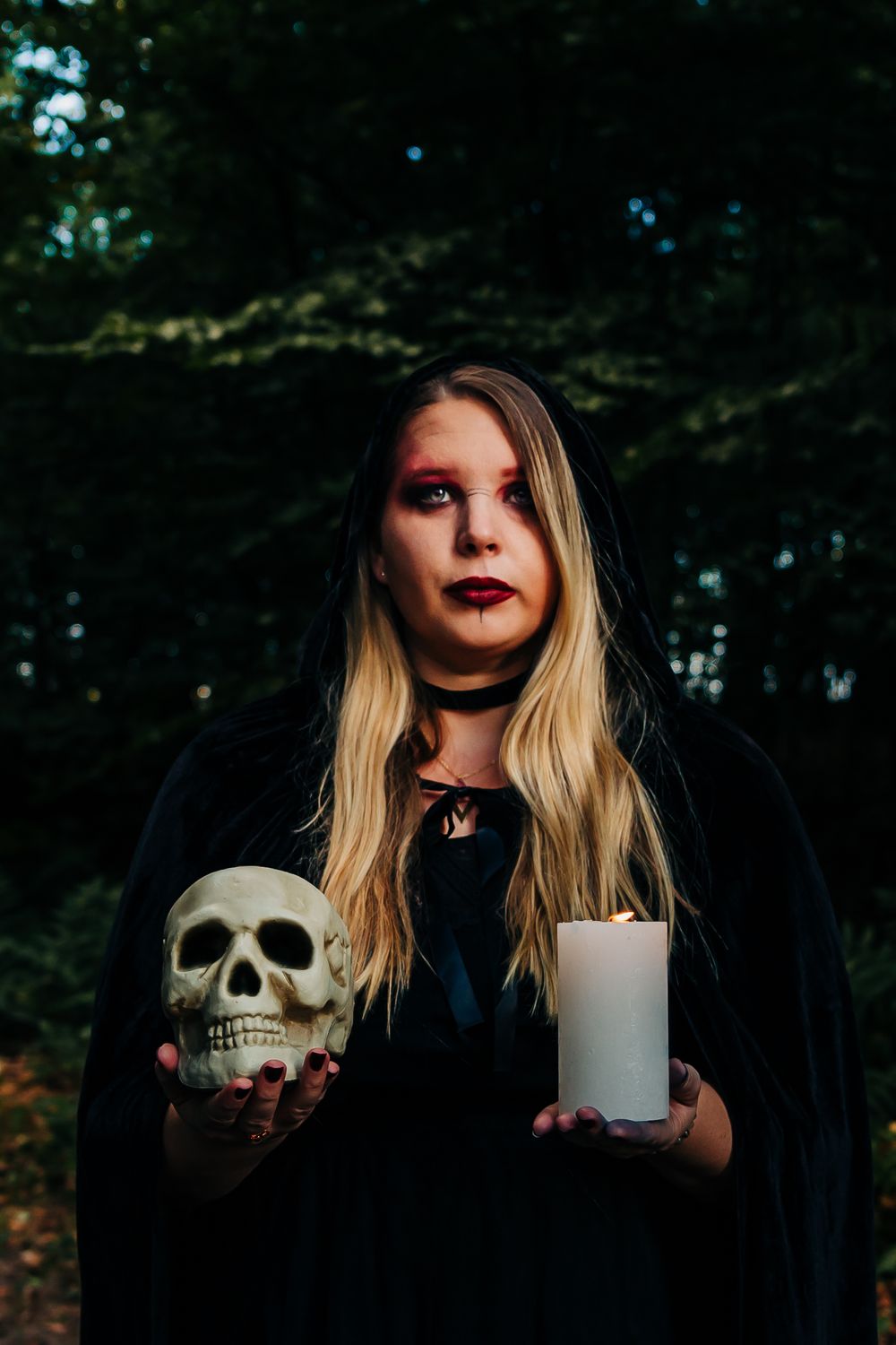 Moody forest portrait featuring black clothing, white candle and decorative skull prop.