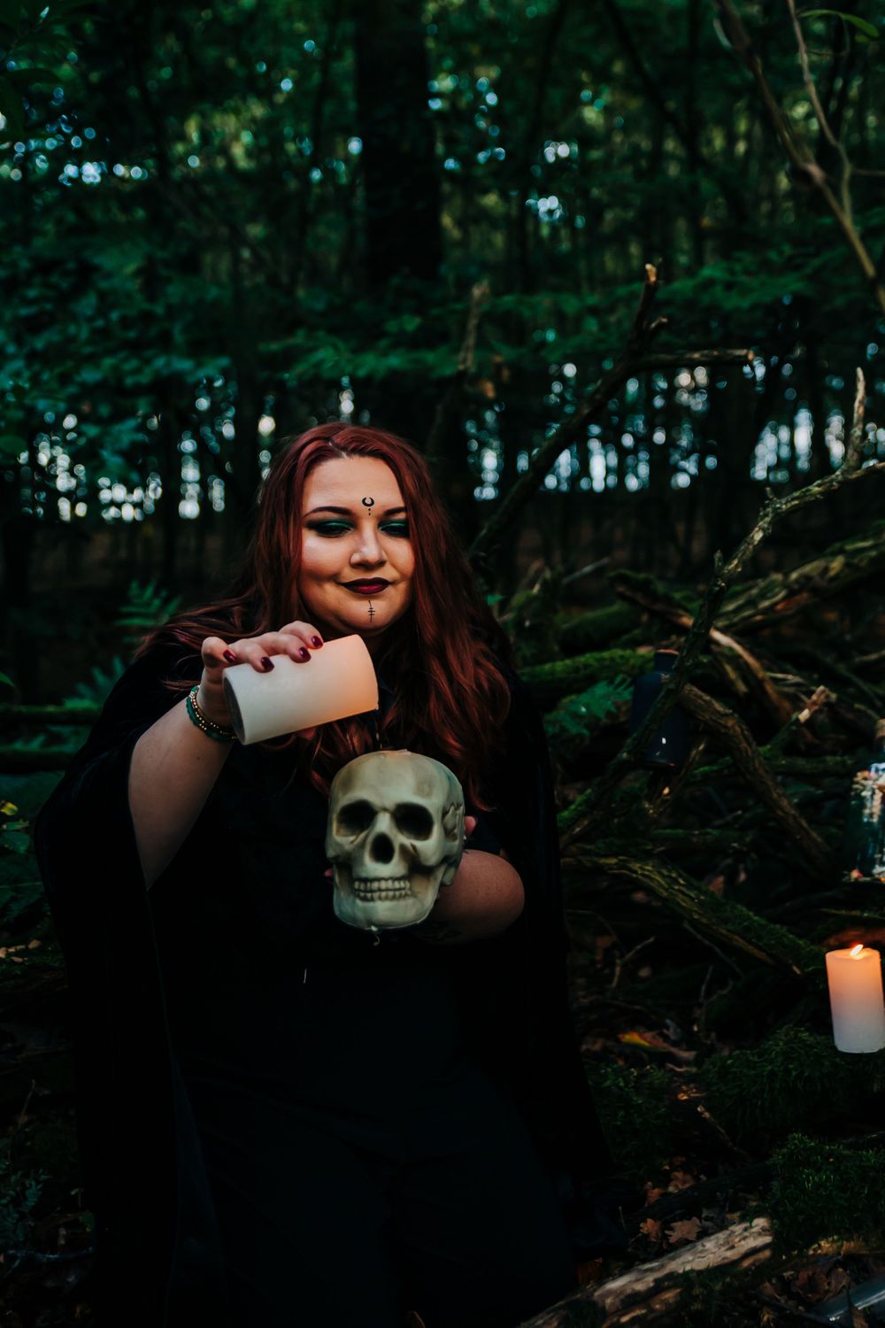 Dramatic forest photoshoot with gothic elements including candles and skull decorations.