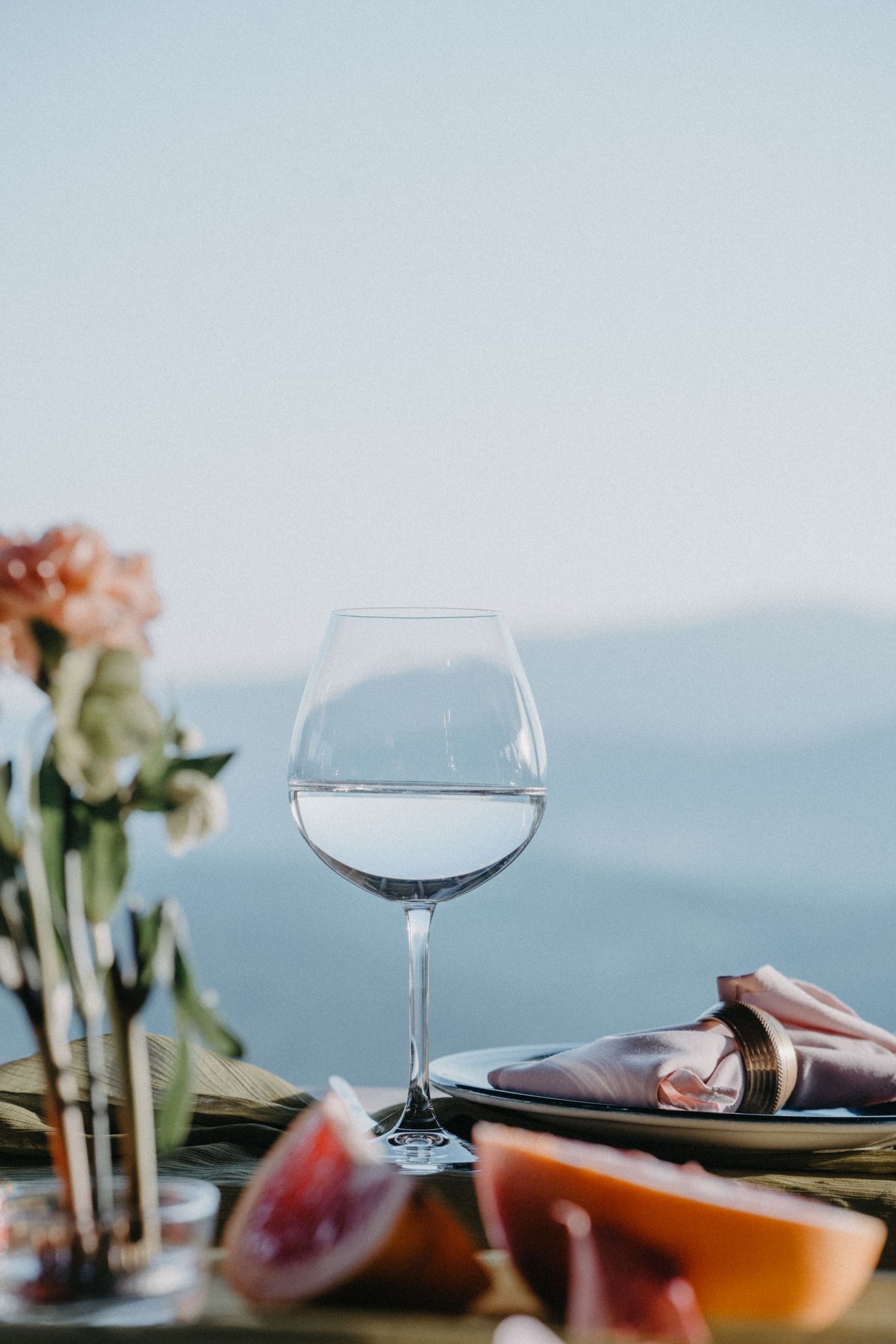 Elegant wine glass filled with water on outdoor dining table with mountain view and fresh flowers.