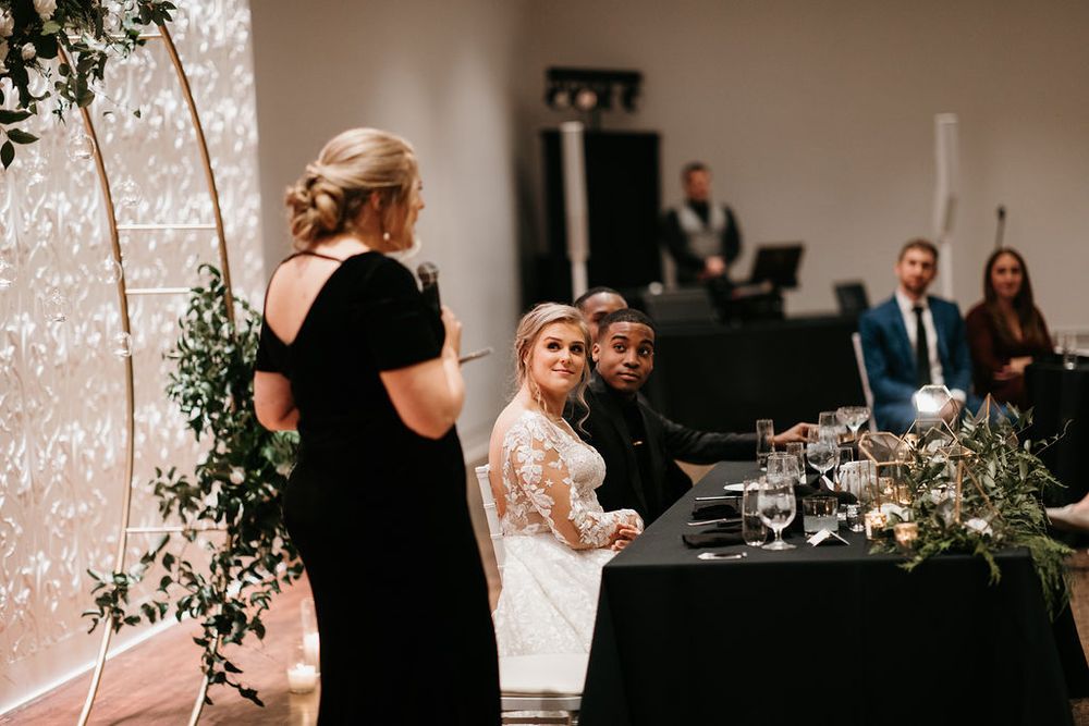Woman giving a toast speech at an elegant wedding reception while the bride and groom listen at the sweetheart table.