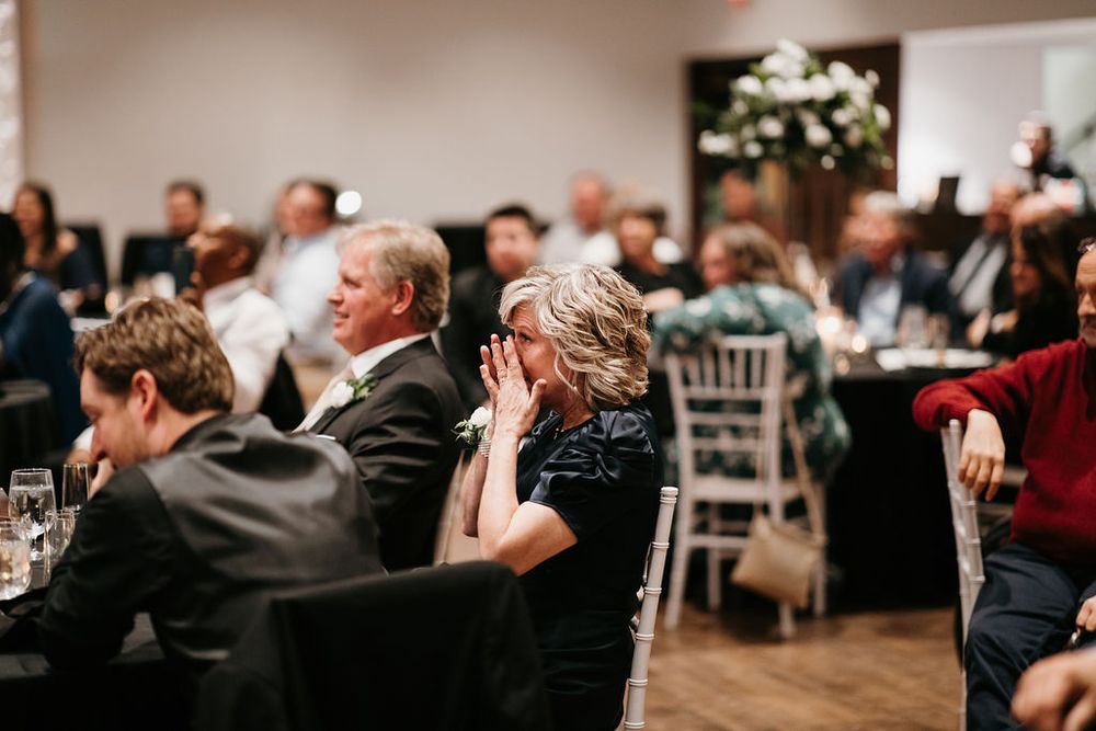 Wedding reception guests seated at tables, with an emotional woman wiping tears during the speeches.