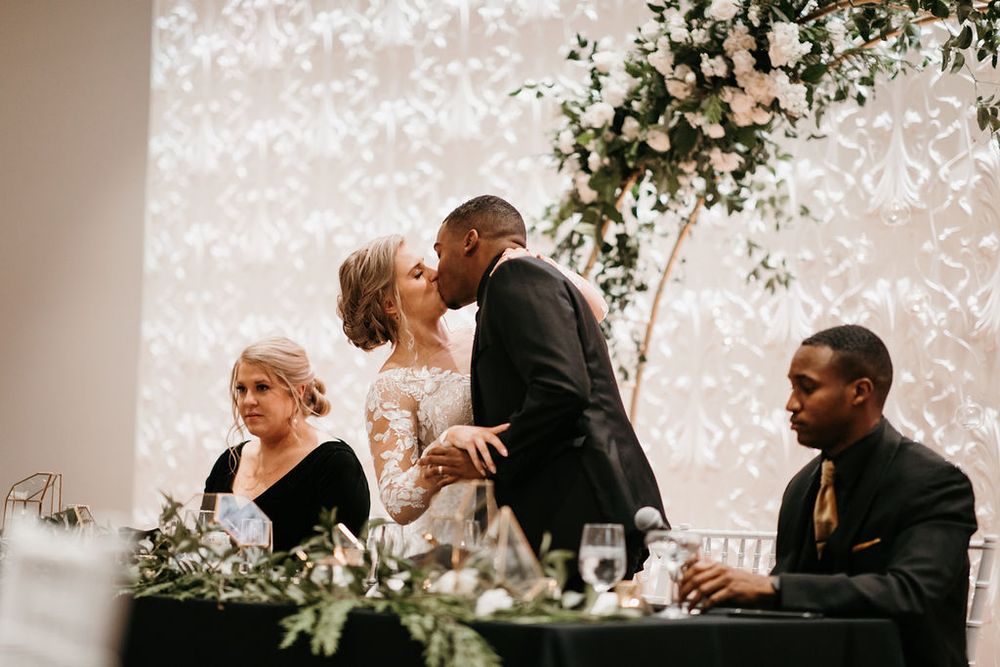 Bride and groom sharing a kiss at the sweetheart table during their wedding reception with floral decor.