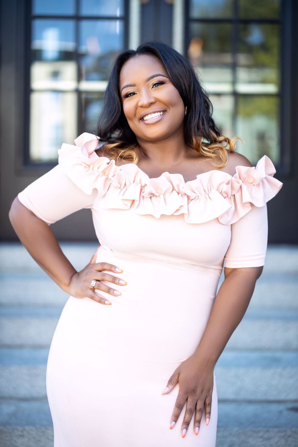 Smiling woman wearing light pink off-shoulder dress with ruffle details.