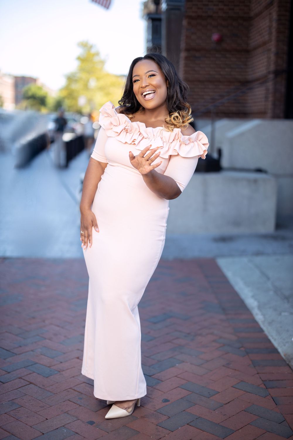 Woman in pink maxi dress laughs joyfully while walking on brick pathway.