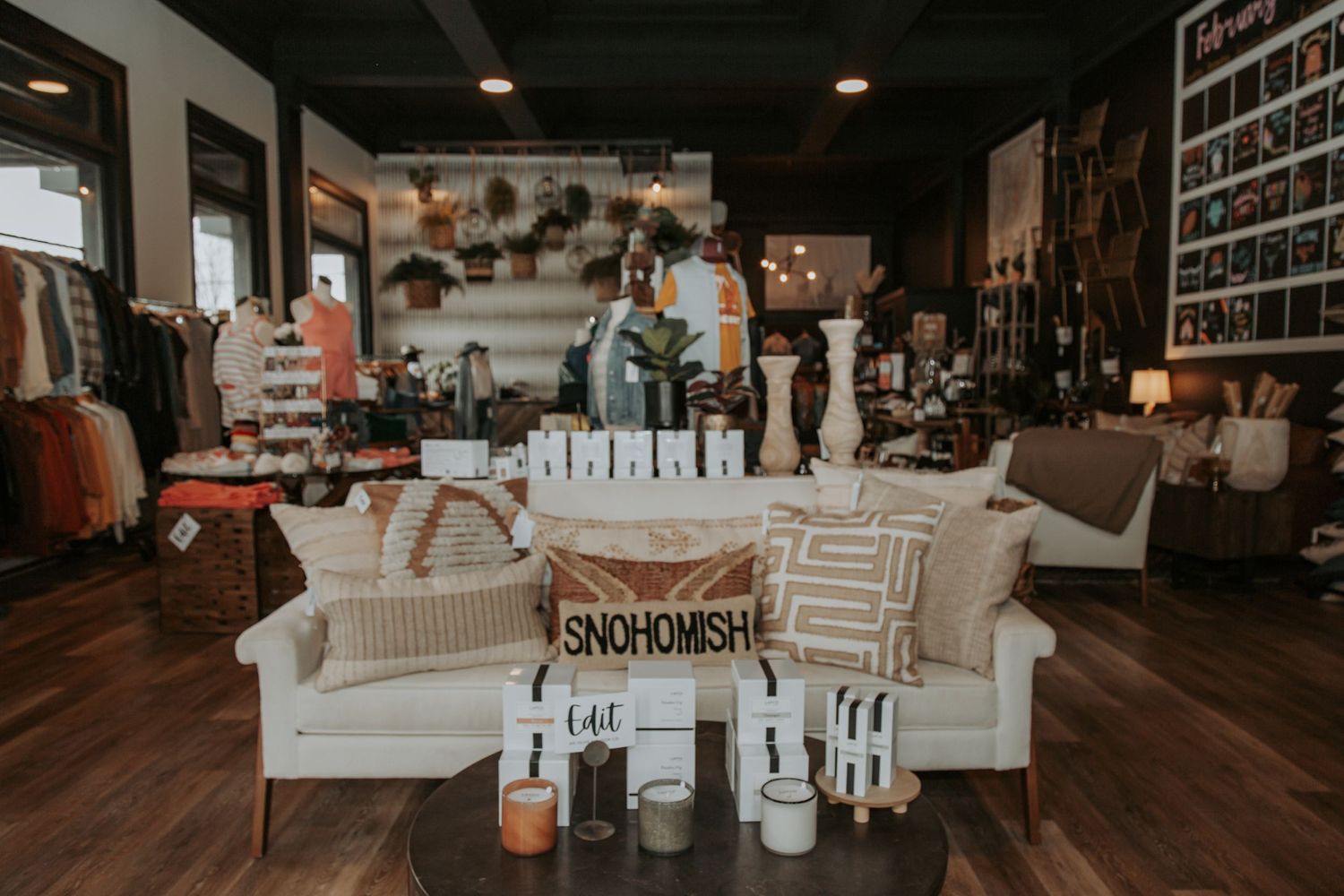 Boutique shop interior with a cream sofa, decorative pillows, candles, plants, and home decor displayed on a wood floor.