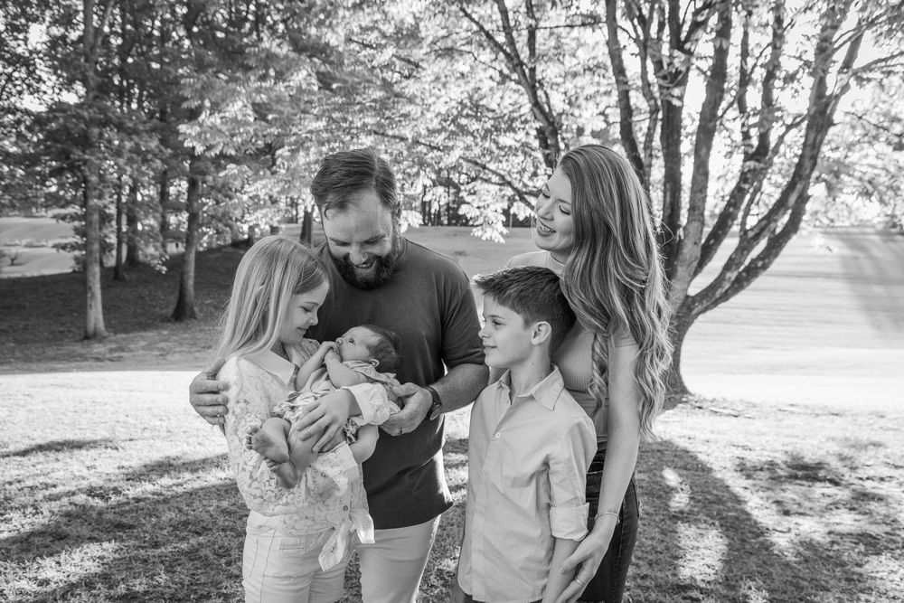 Family photoshoot in a park setting with natural lighting and trees.