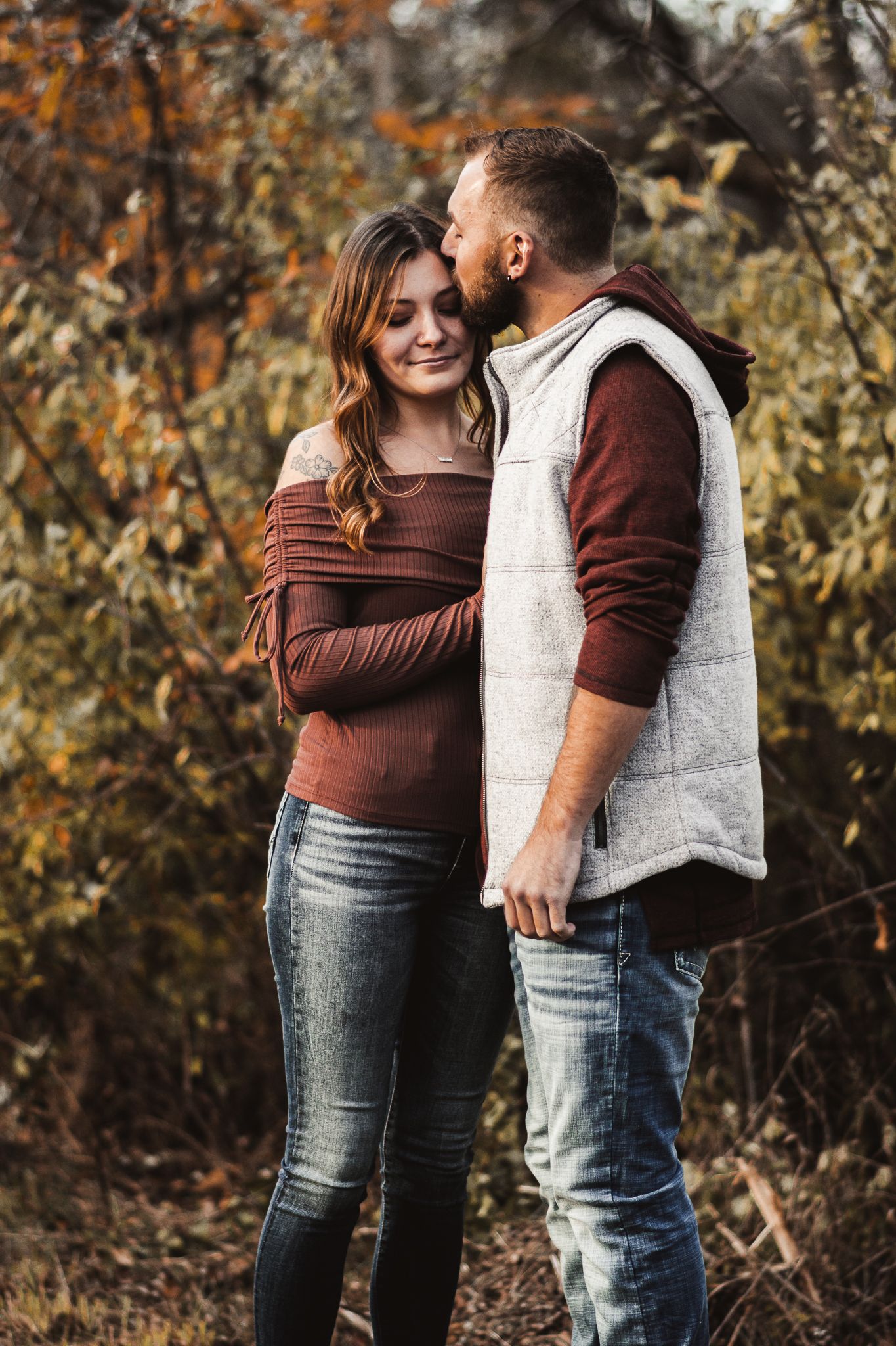 Fall engagement photo with couple in coordinated casual wear against autumn foliage.
