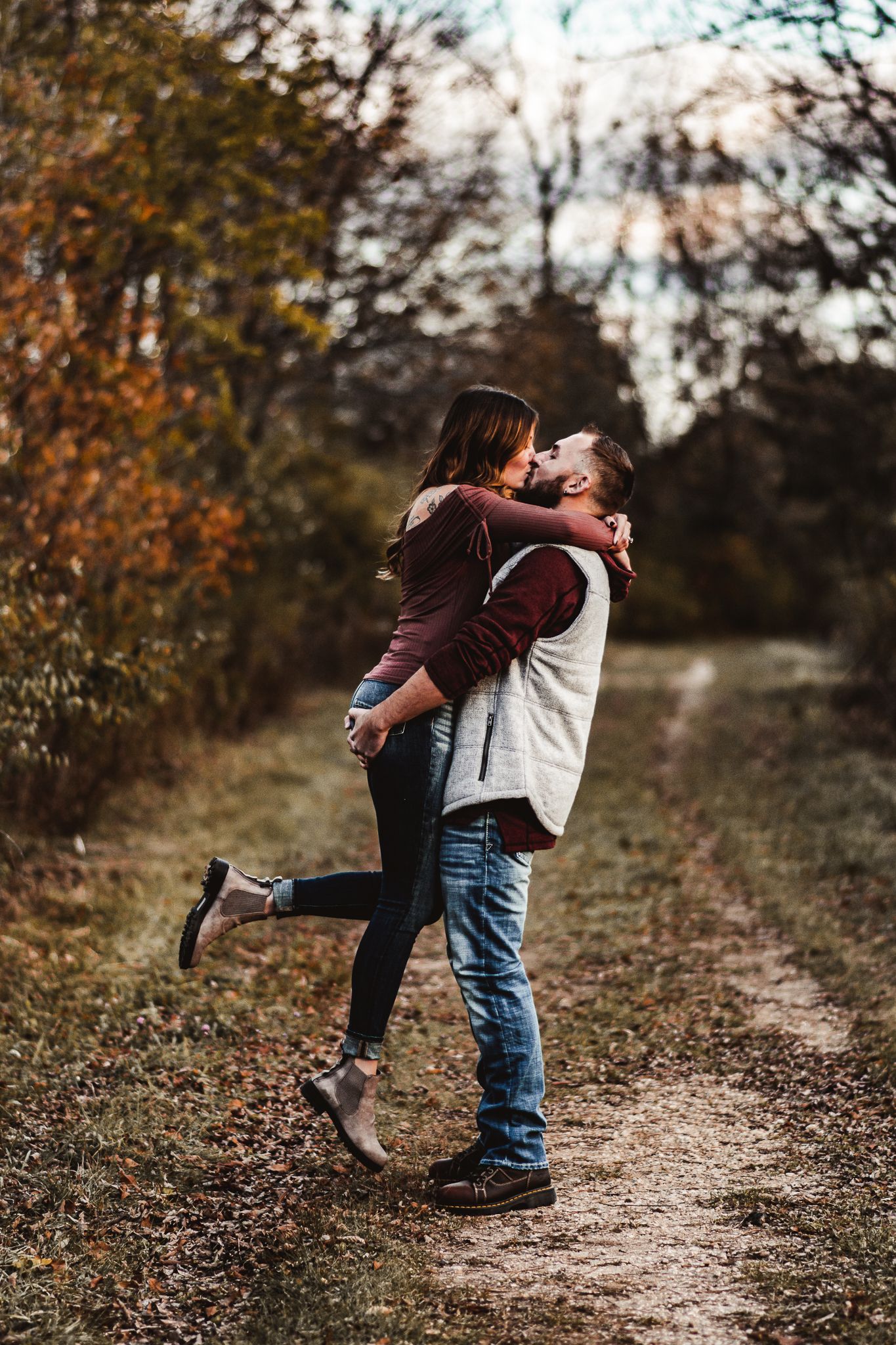 Playful engagement photo of couple embracing on a fall forest path.