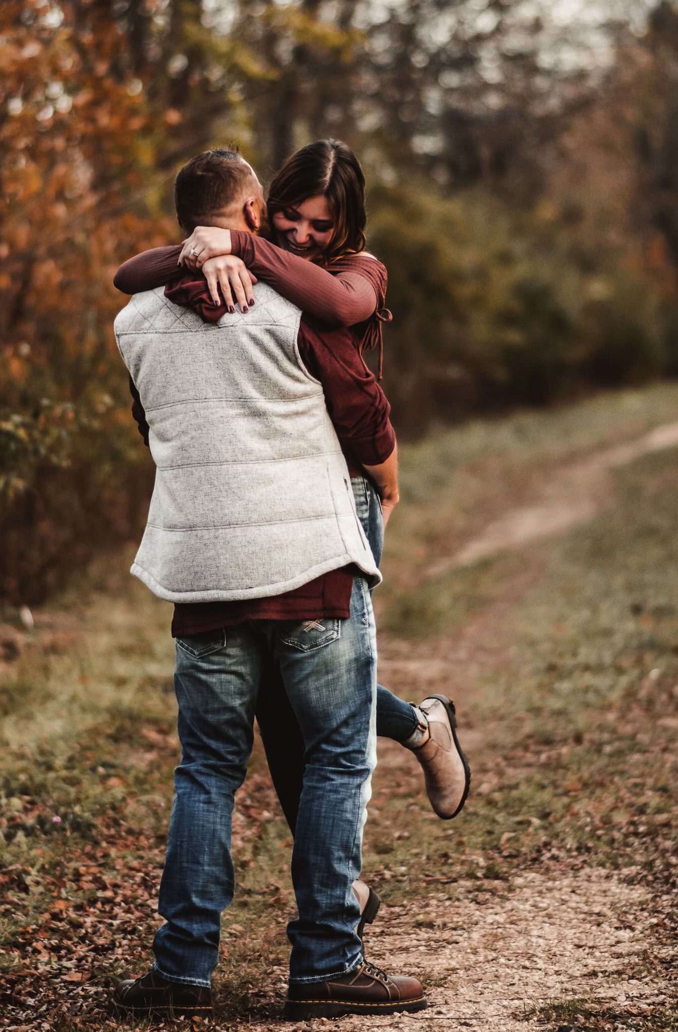 Couple embracing on a fall trail with autumn foliage in the background.