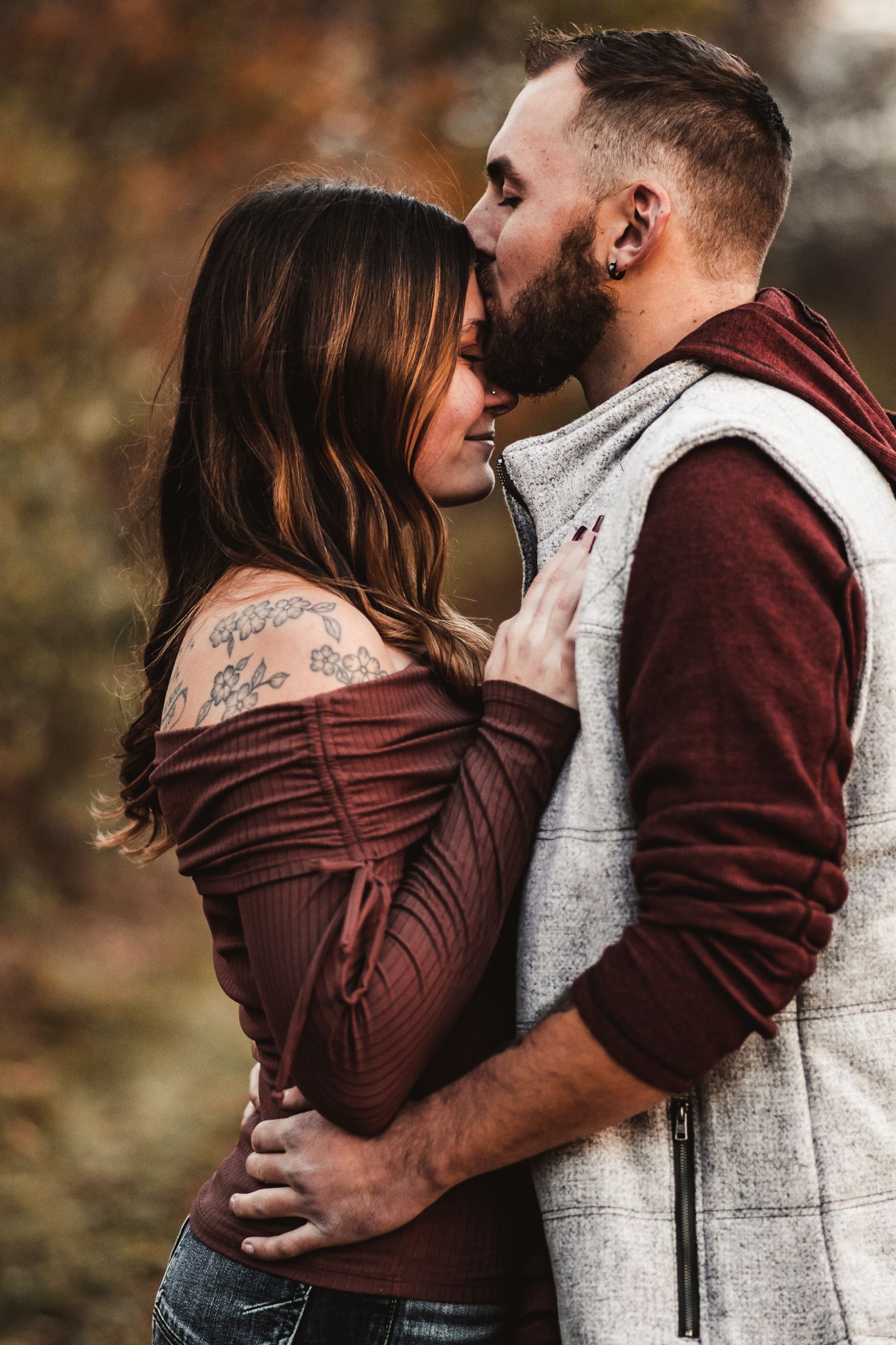 Intimate couple moment captured in burgundy and grey clothing against fall foliage.