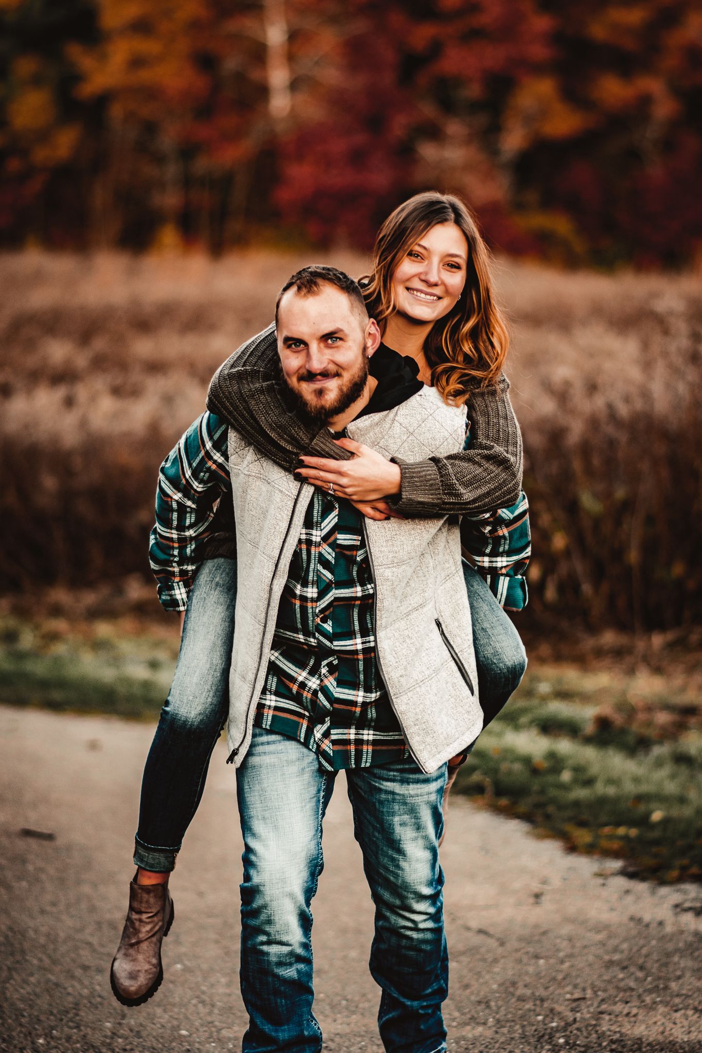 Playful piggyback ride moment during fall photoshoot with couple in casual wear.