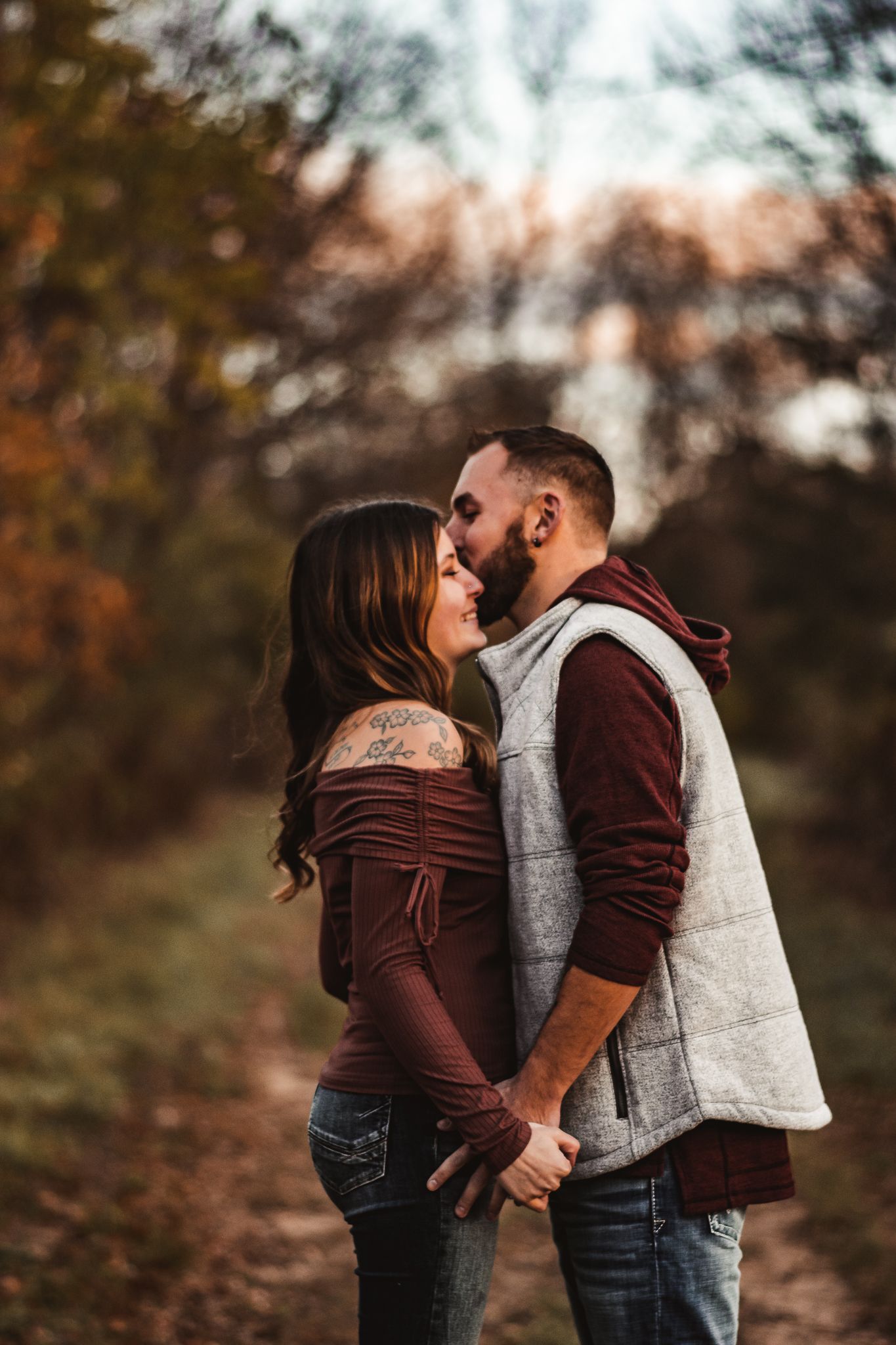 Romantic autumn portrait of couple in matching burgundy and grey outfits on woodland path.