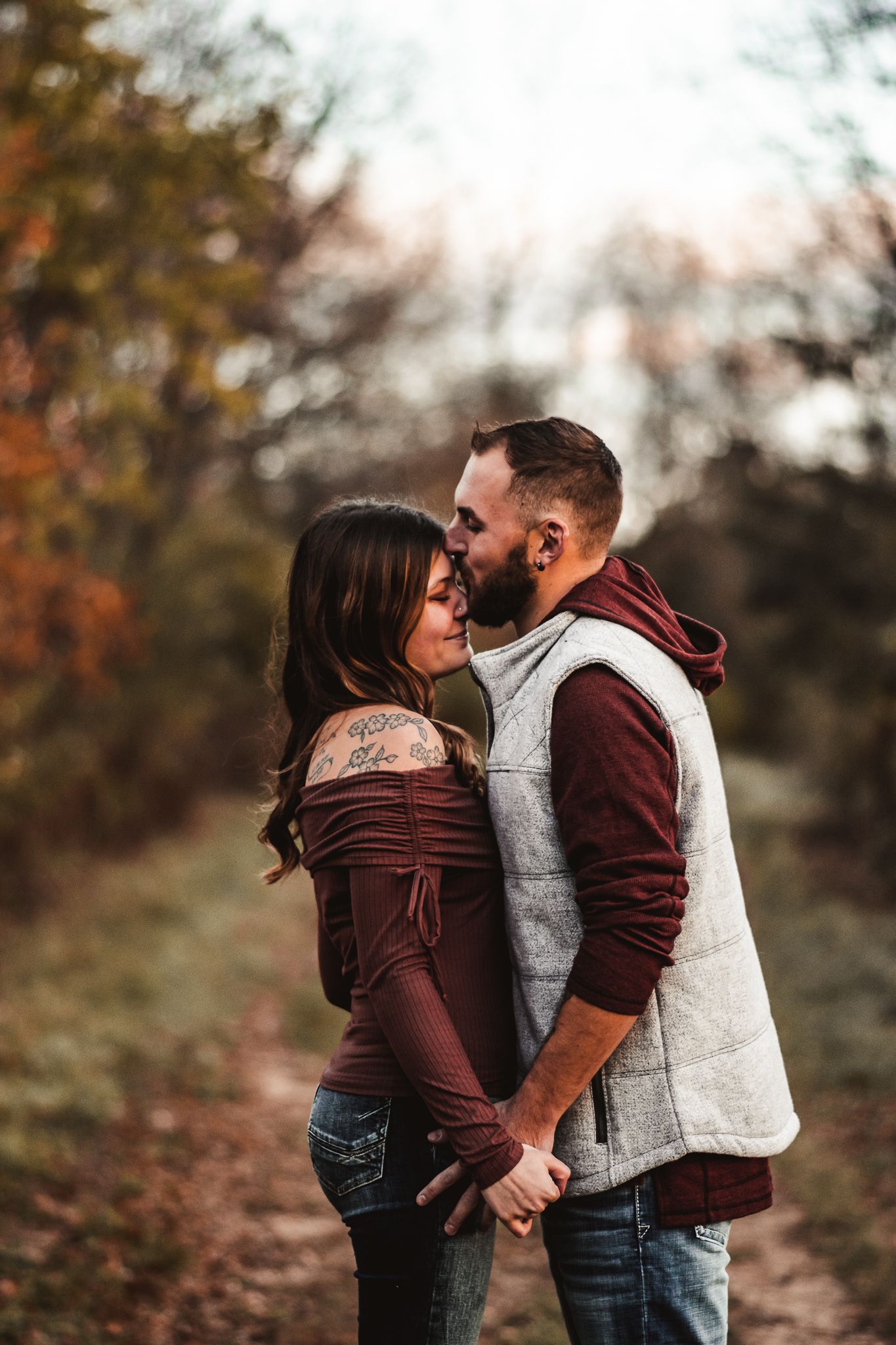 Tender moment between couple in burgundy and grey clothing on autumn trail.
