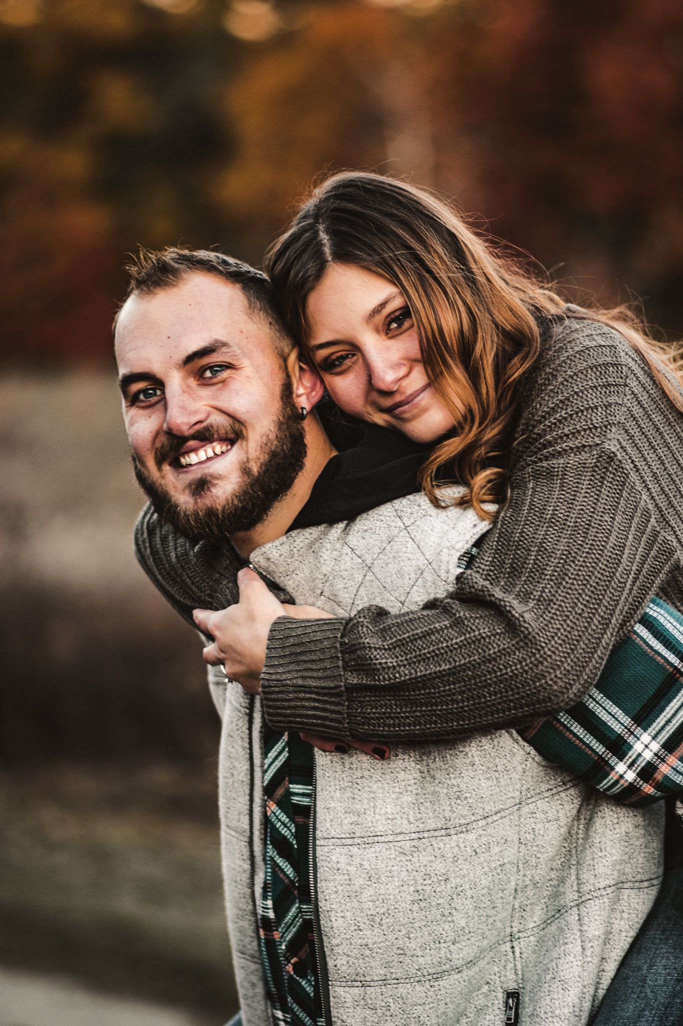 Happy couple sharing laughter during piggyback ride in autumn setting.