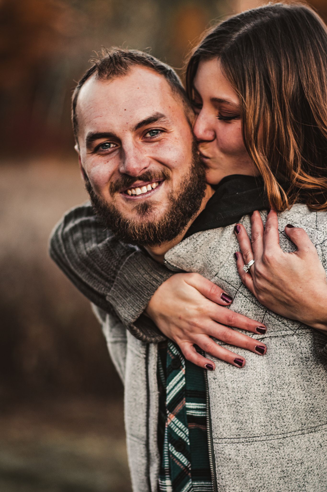 Joyful outdoor portrait of couple sharing embrace in autumn setting.
