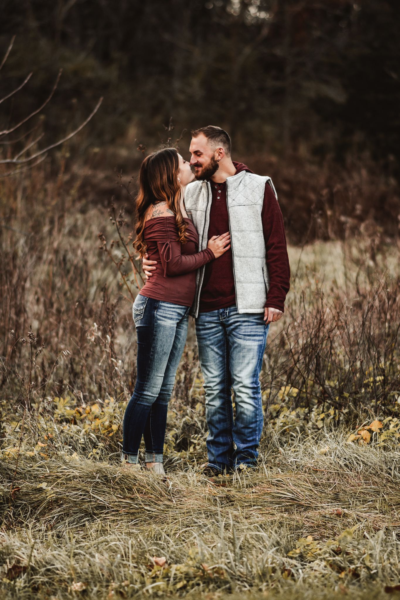 A romantic couple in matching burgundy and white outfits shares an intimate moment in an autumn field.