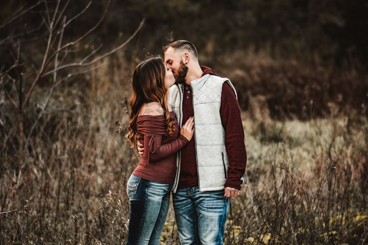 A couple stands close together sharing an intimate moment in a rustic outdoor setting.