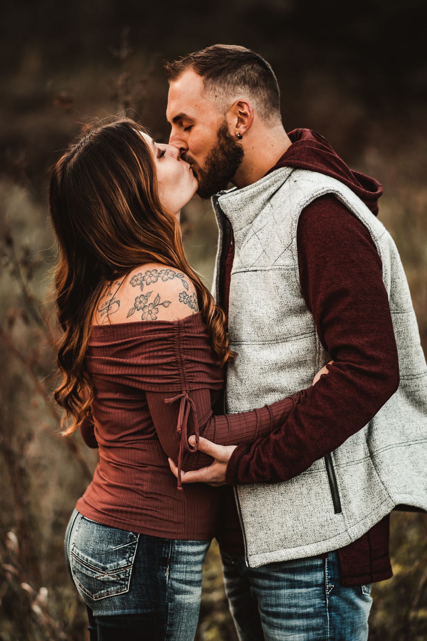 A couple in casual fall clothing shares a romantic kiss during their outdoor photo session.