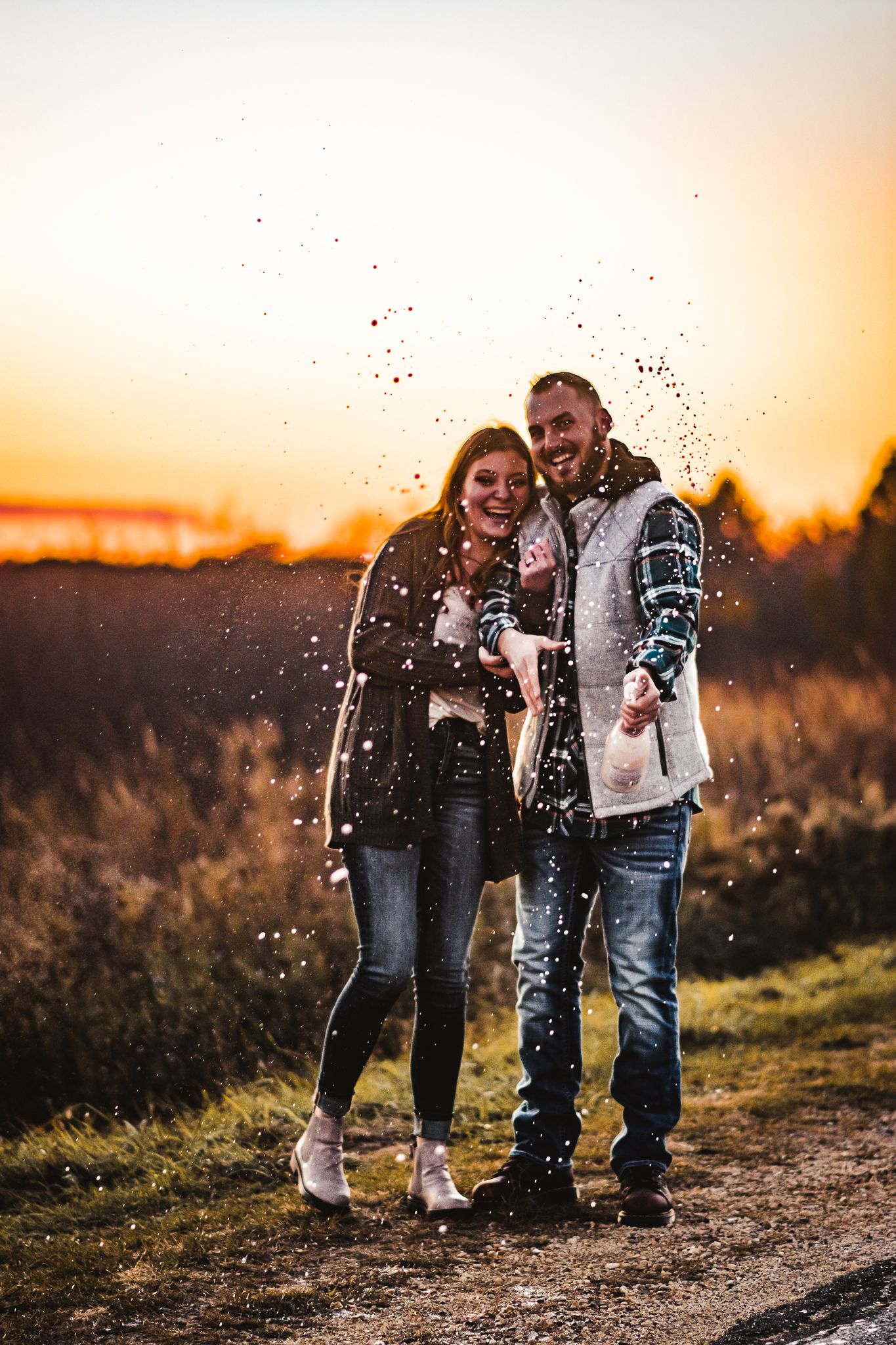 A joyful couple laughs together as sparkles fall around them during a sunset photoshoot.