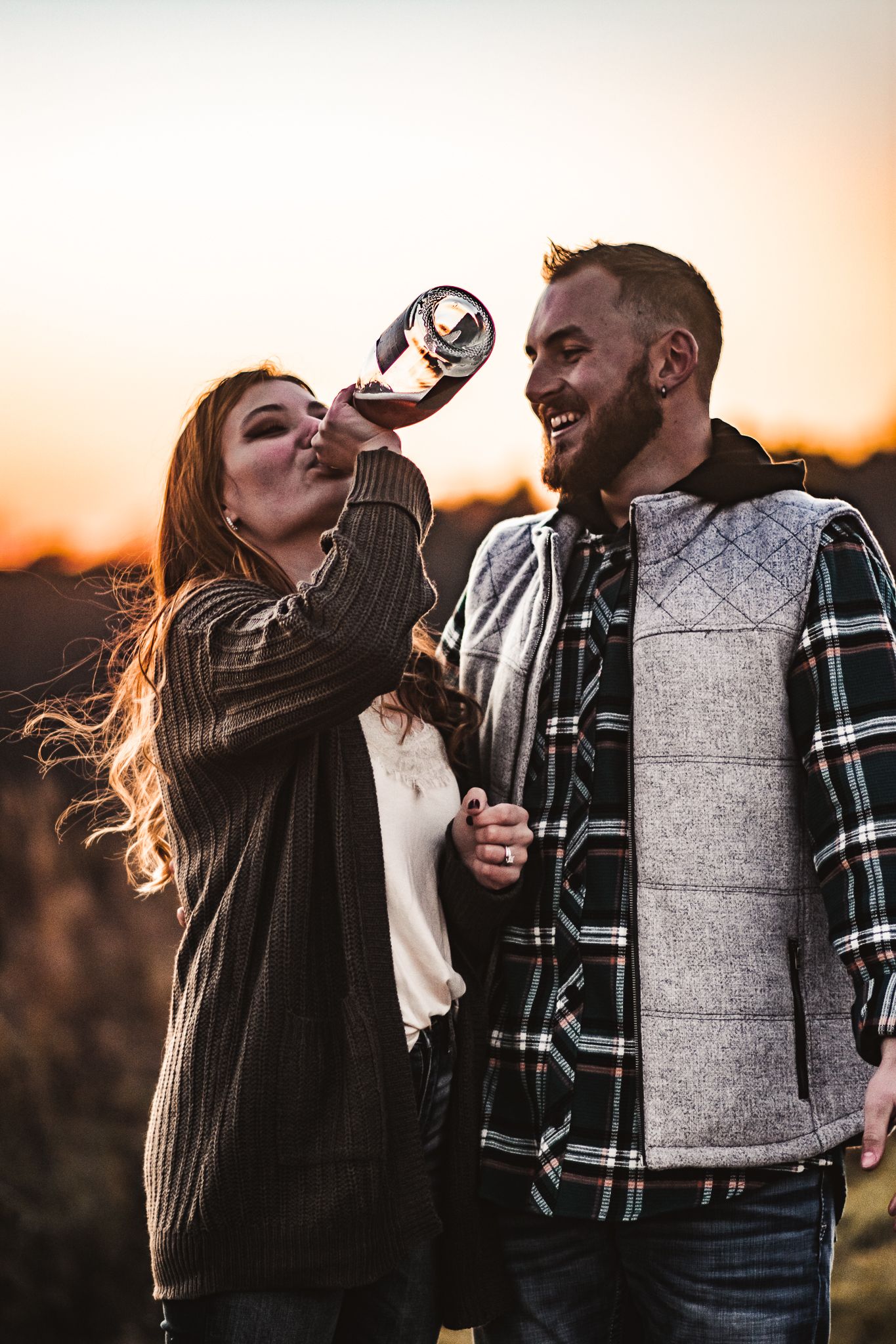 Couple sharing a romantic drink at sunset while wearing casual fall outfits.