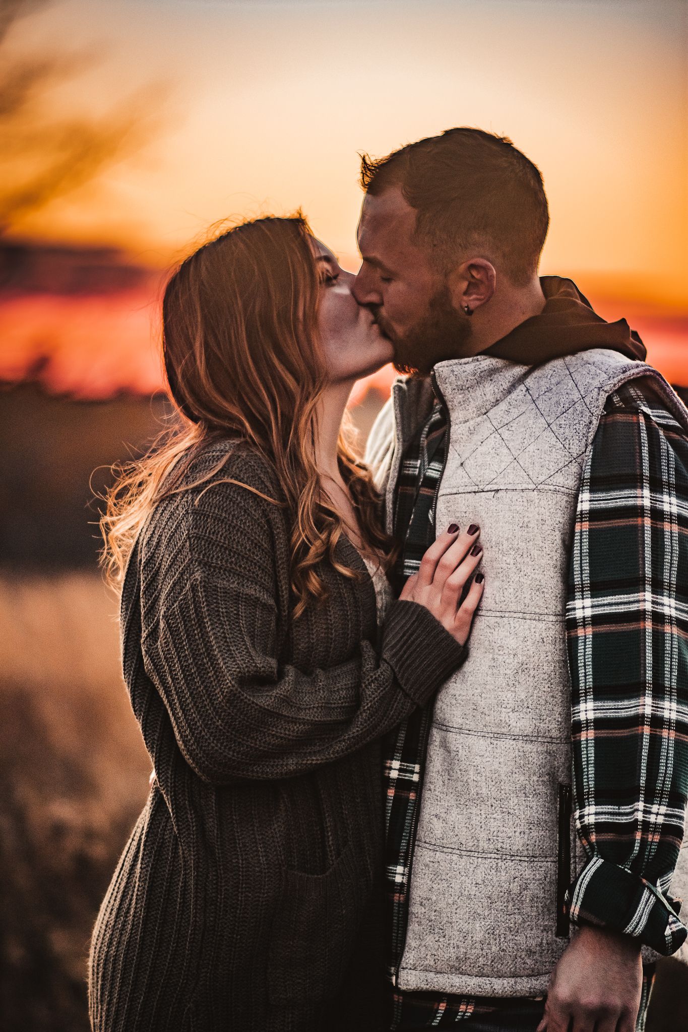 Romantic sunset kiss between couple in warm winter clothing.