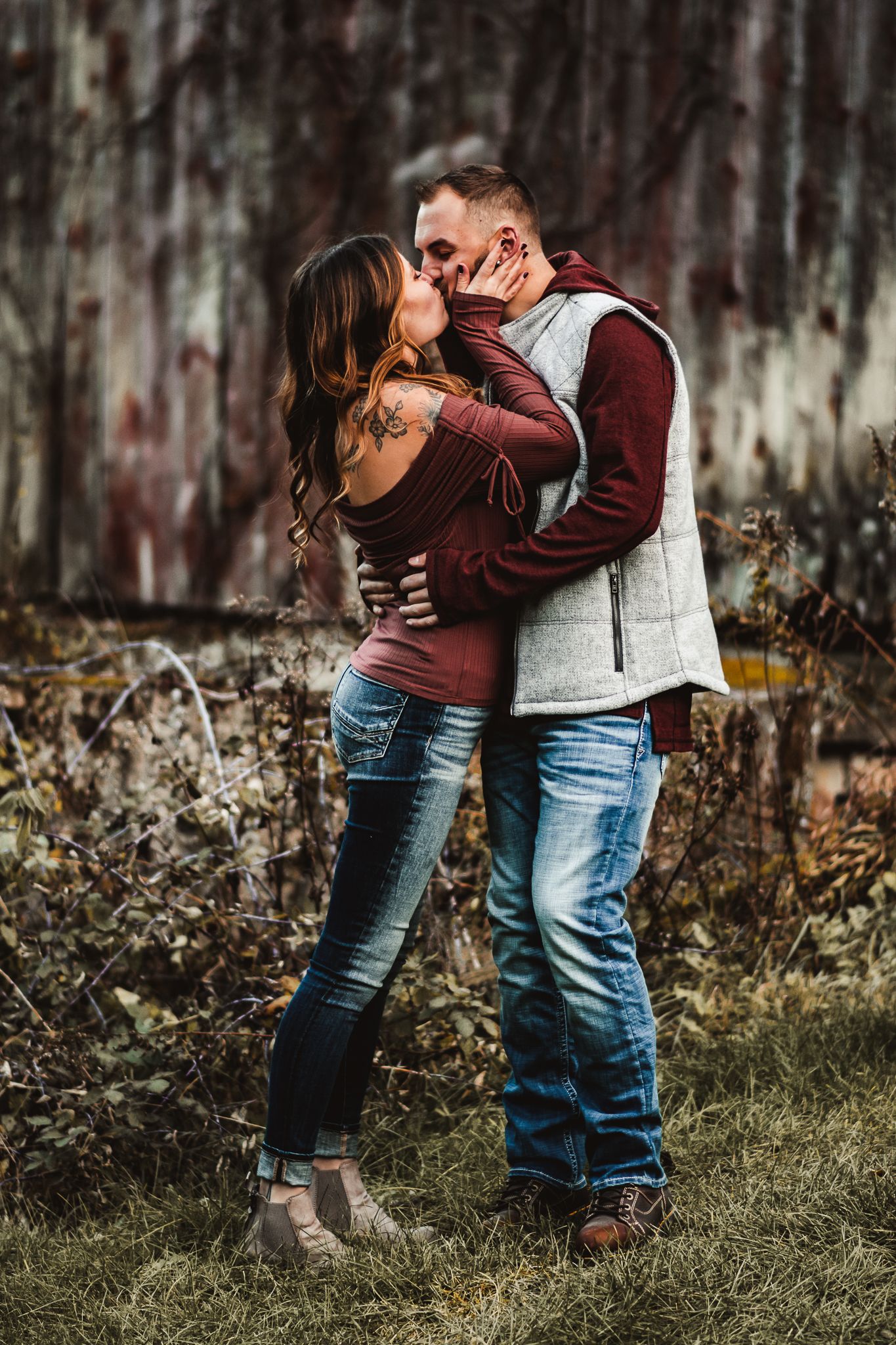 Playful romantic moment between couple in matching burgundy and grey outfits outdoors.