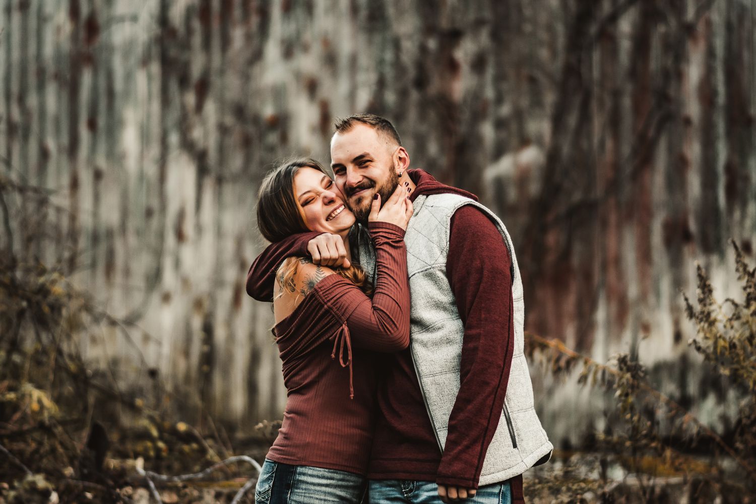 Joyful couple laughing together during outdoor autumn photoshoot near rustic wall.