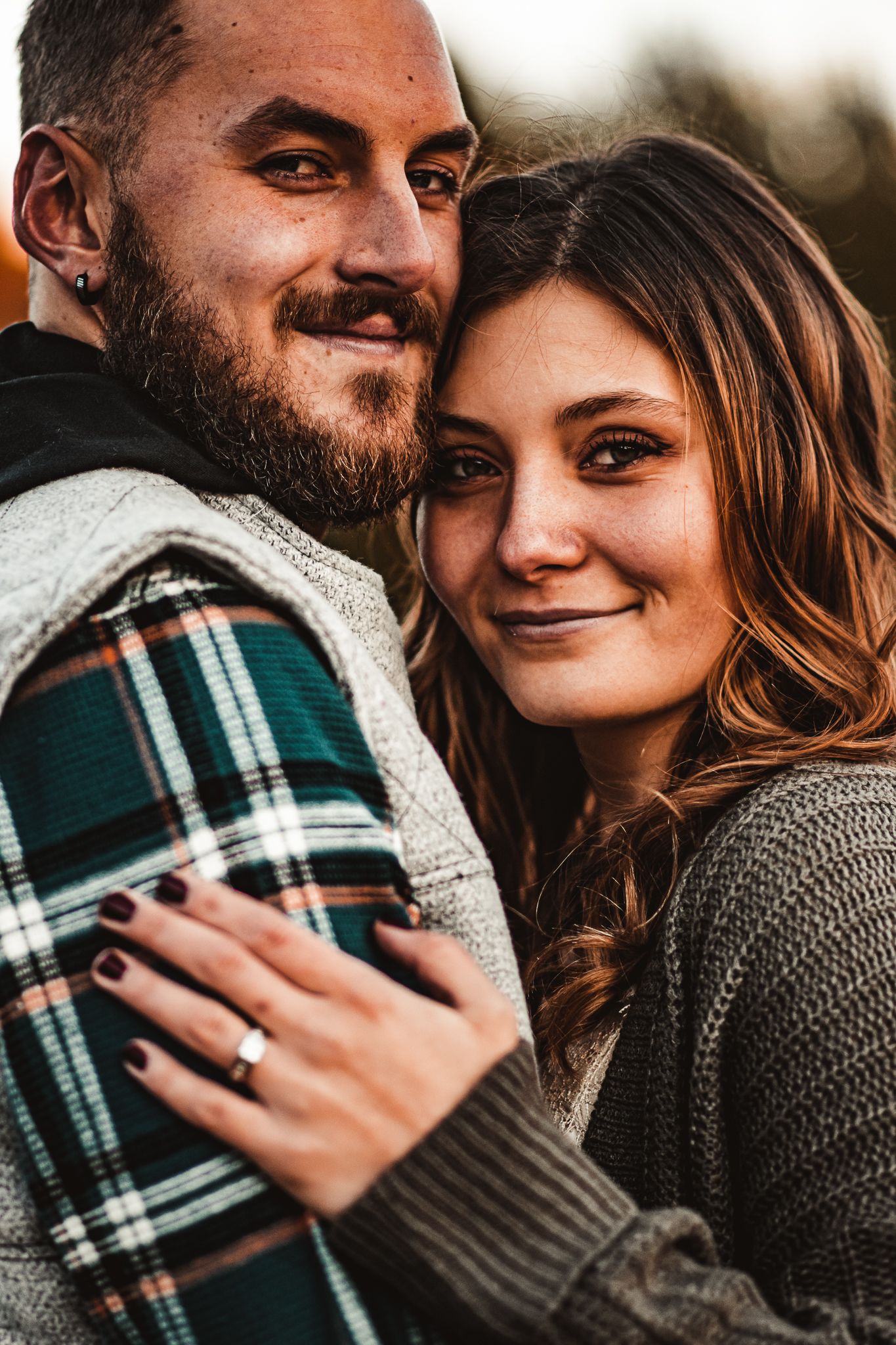 Close-up autumn engagement photo showing couple in plaid and knit sweaters.