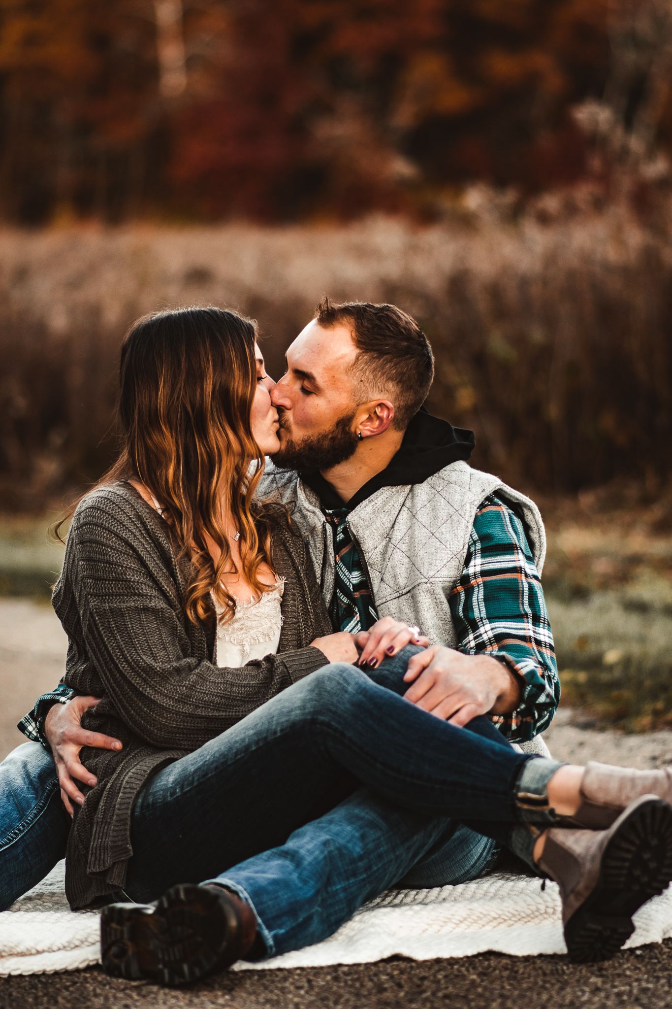 Couple cuddling on blanket during romantic fall picnic with autumn foliage in background.