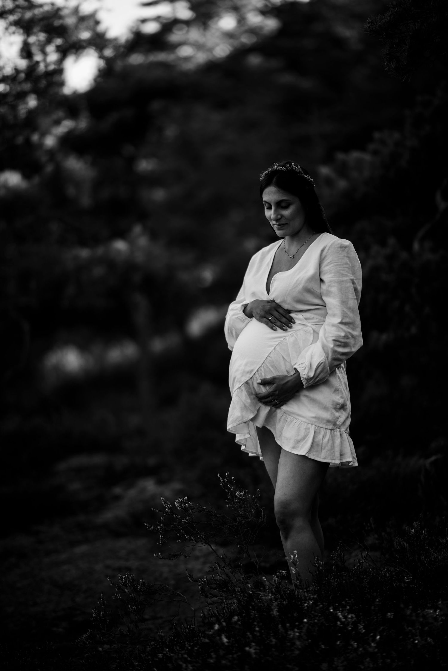 A silhouetted figure in a white dress stands outdoors during pregnancy.