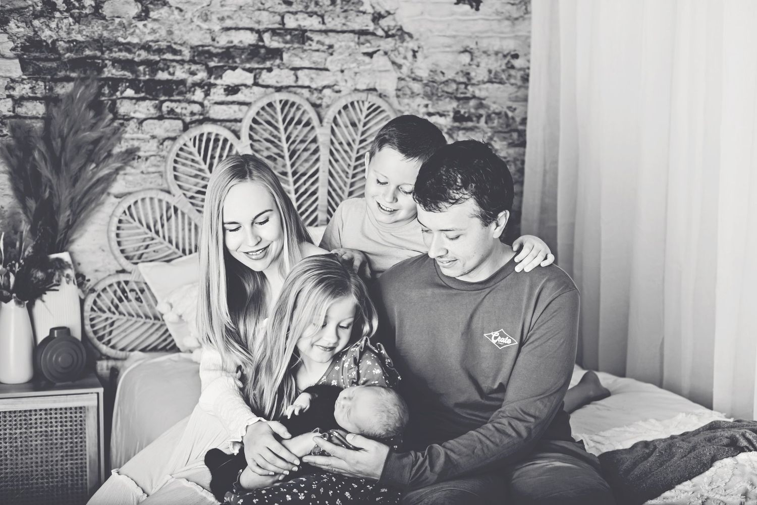 Black and white photo of family sharing joyful moment together on wicker headboard bed.
