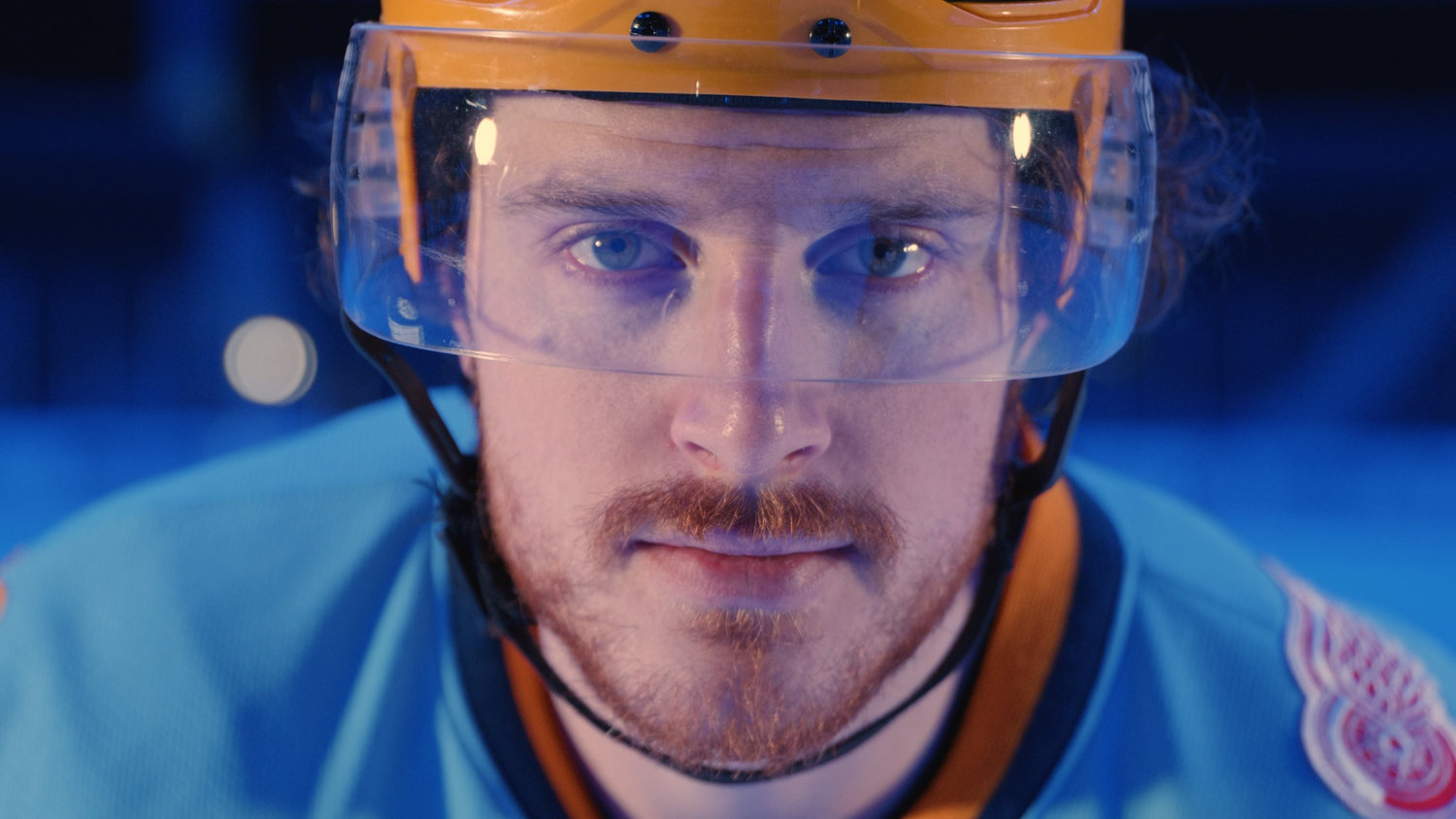 Close-up profile of hockey player wearing orange helmet against blue background.