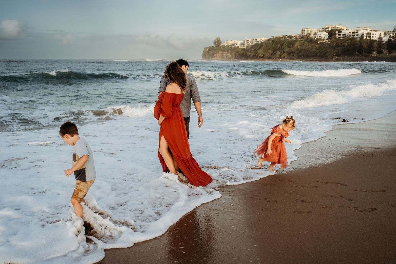 Family playing in ocean waves on tropical beach at sunset.