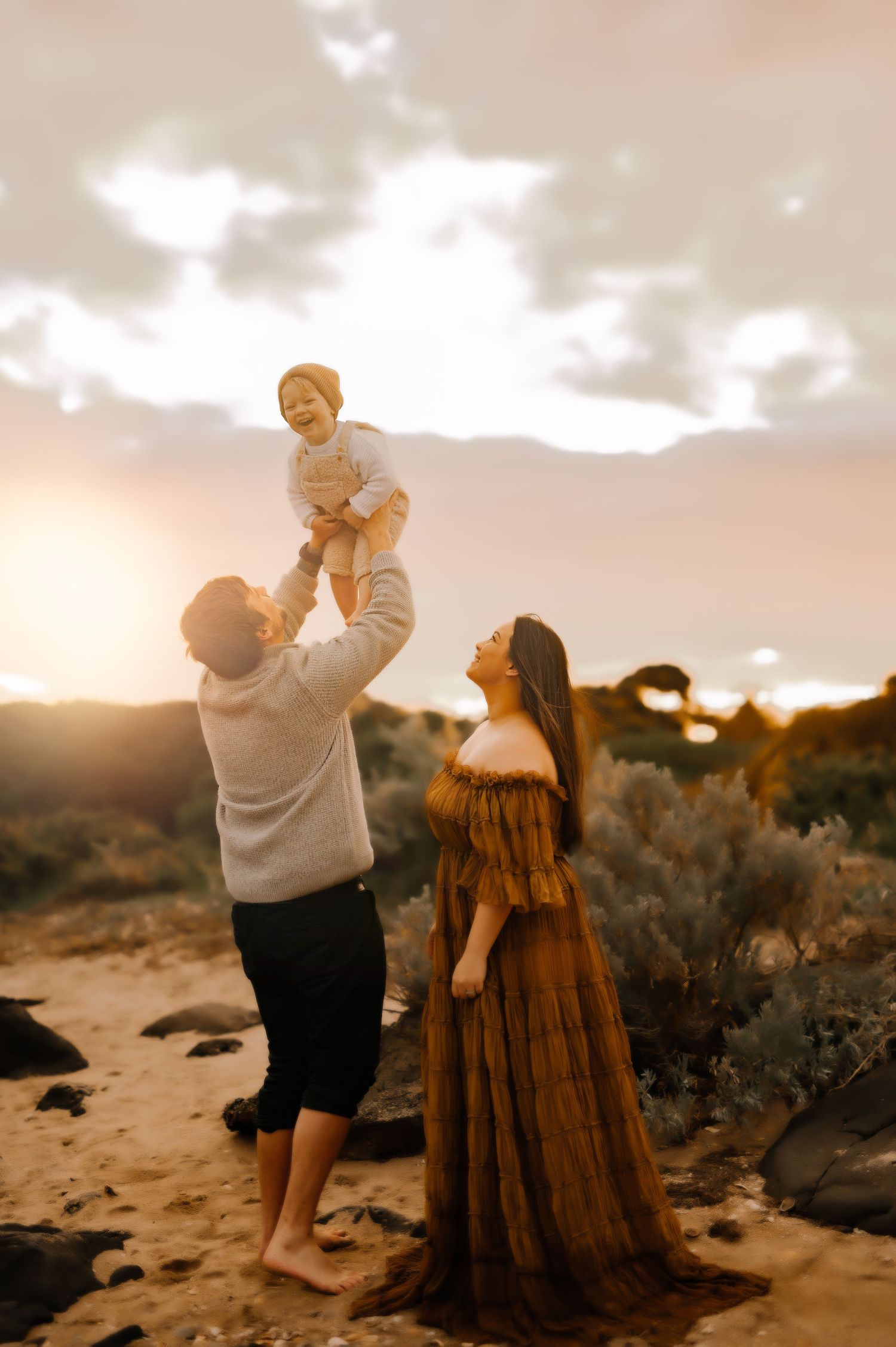 A family shares a tender moment against a sunset backdrop on a rocky beach.