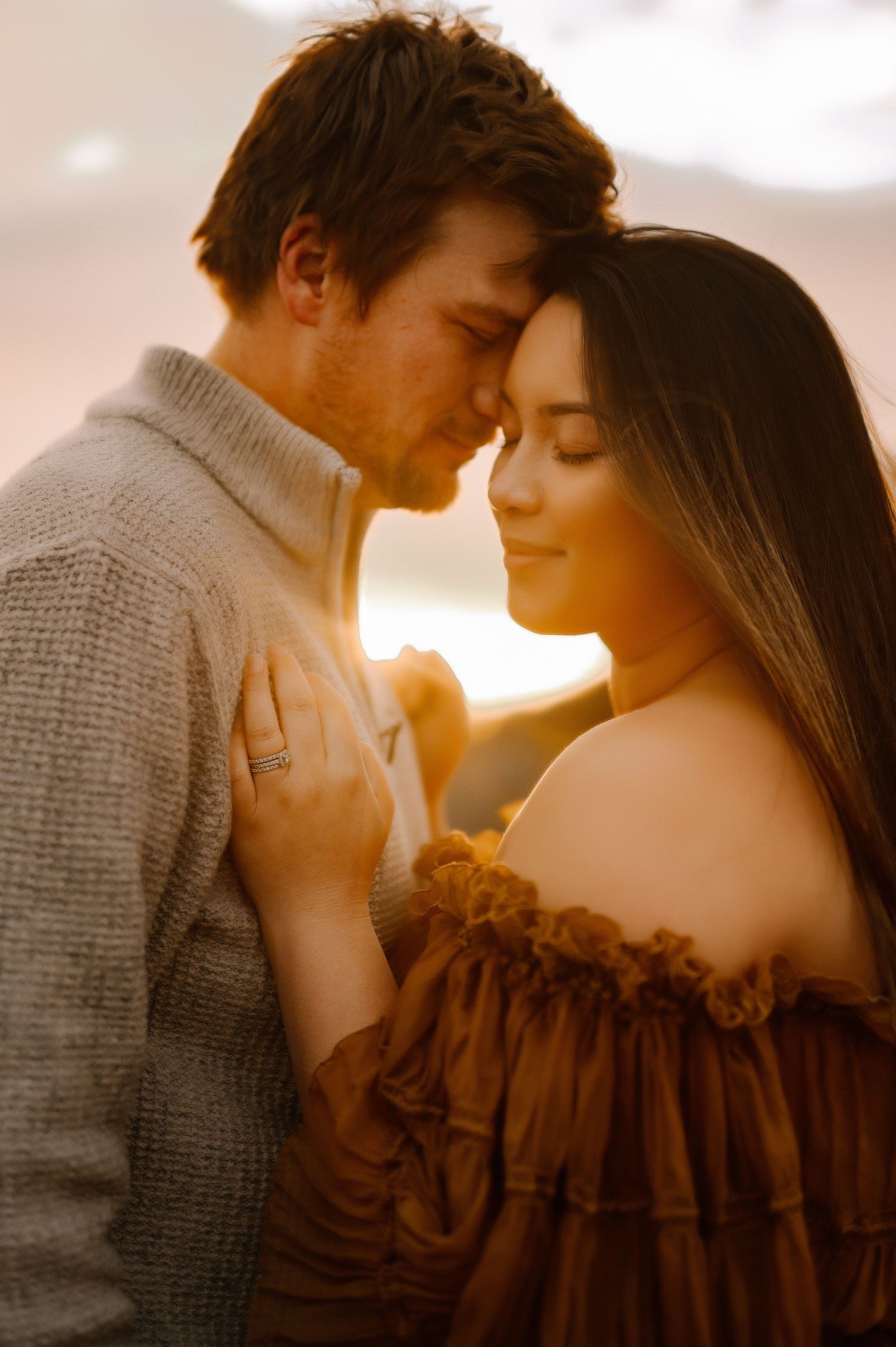 An intimate couple's portrait captured in golden hour light against a coastal backdrop.
