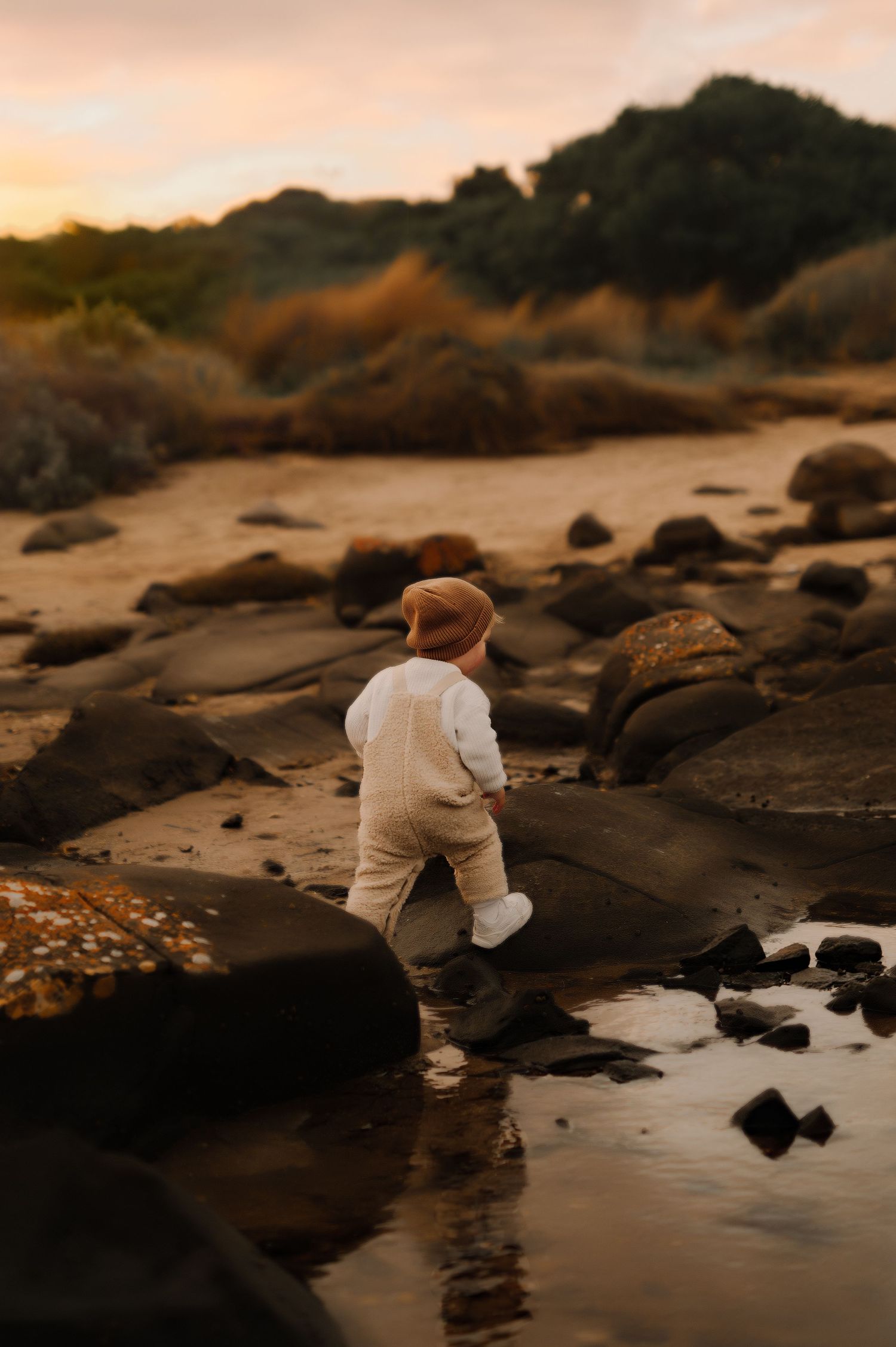 A small child explores rocky coastal terrain during a golden sunset.