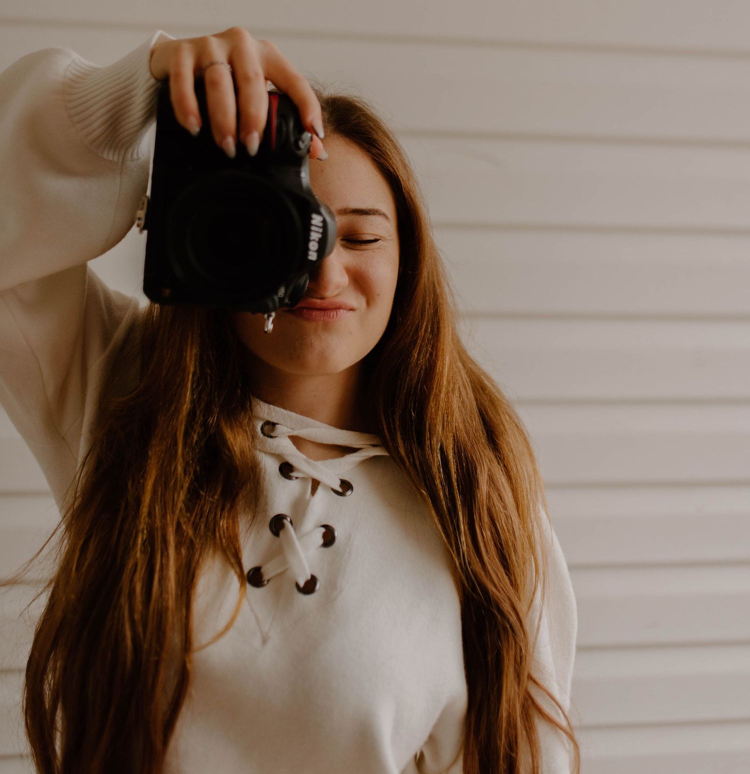 Person taking photo with black camera while wearing cream colored sweater with lace-up neckline.