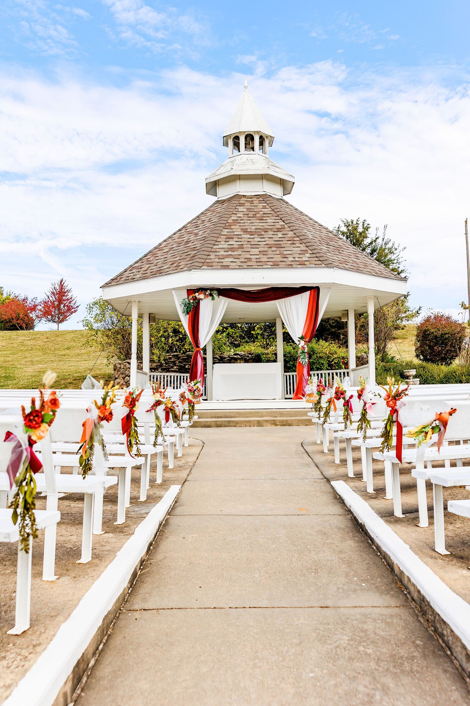 White gazebo decorated with red drapes and floral arrangements for outdoor wedding ceremony by Stephanie Coulter Photography