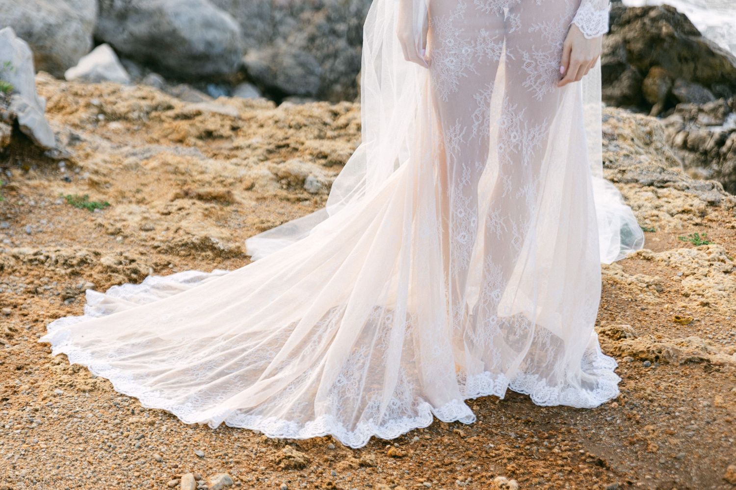 Close-up of a flowing white wedding dress train on rocky terrain.
