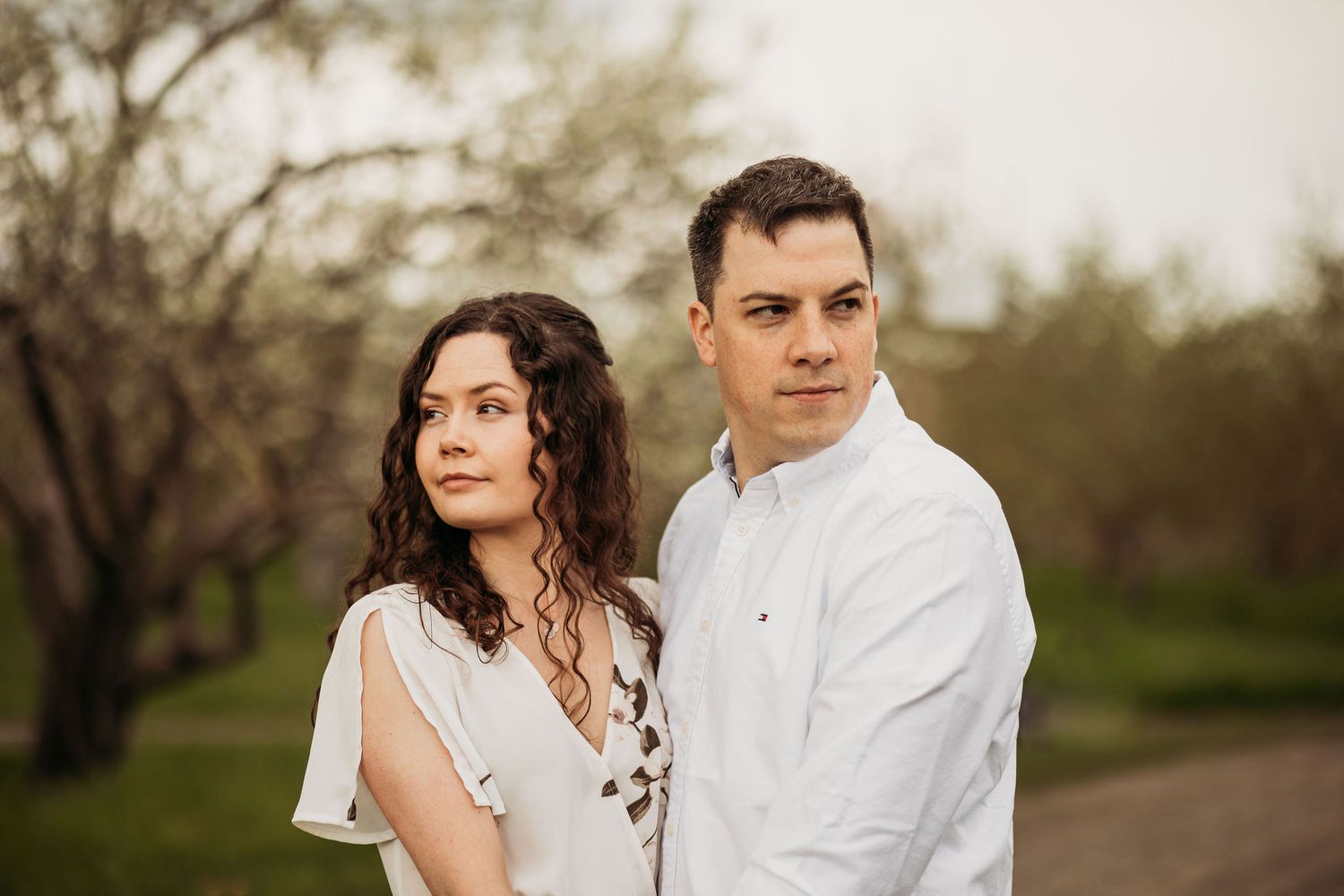 A couple stands close together against a backdrop of blossoming spring trees at sunset.