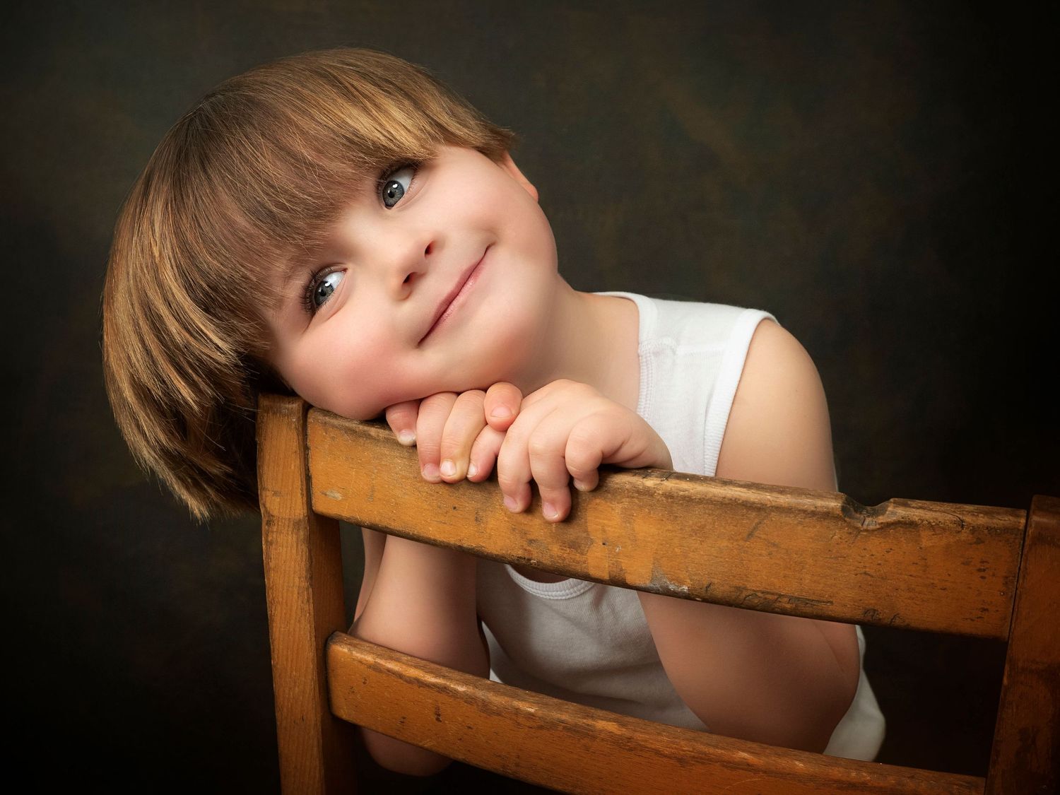 portrait of a 3 year old boy sitting on a wooden chair with a smile