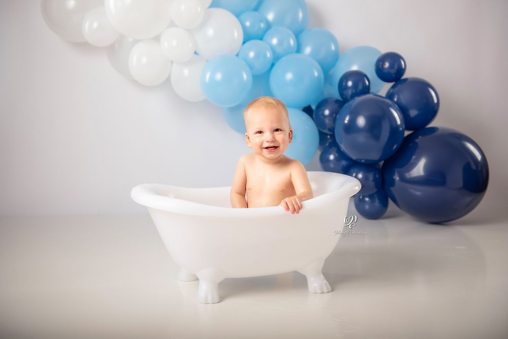 Smiling baby boy in small tub with shades of blue balloon arch Cake Smash session; Lexington, SC photographer; 1st bday