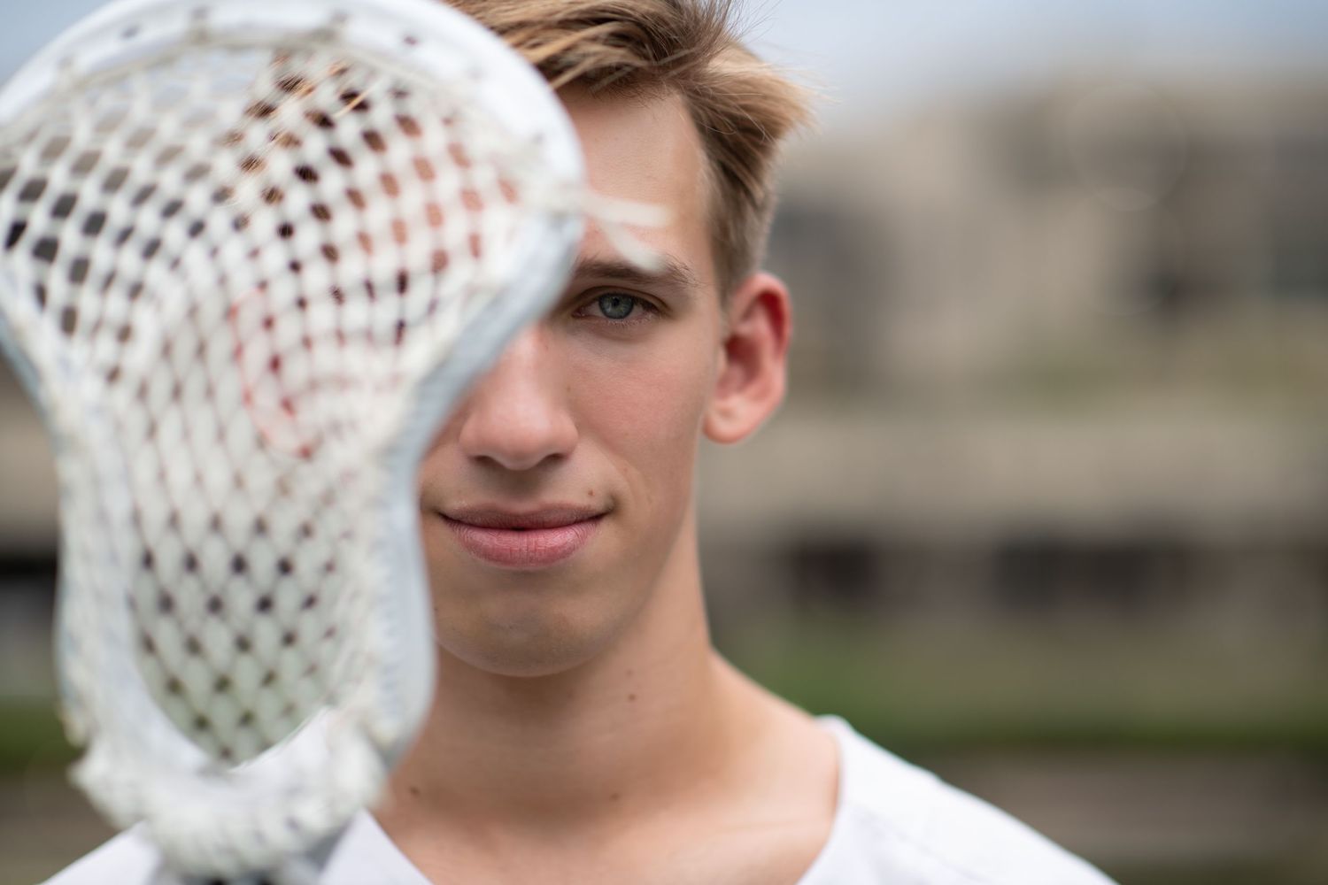 senior boy holding lacrosse stick half way in front of face looking at camera.