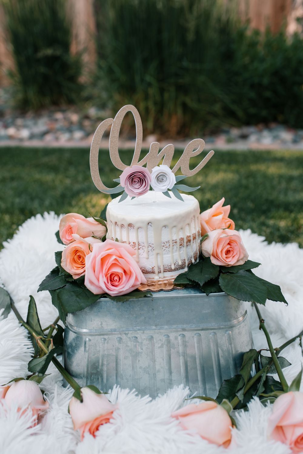 White tiered cake decorated with peach roses sits on galvanized stand with tulle accents.