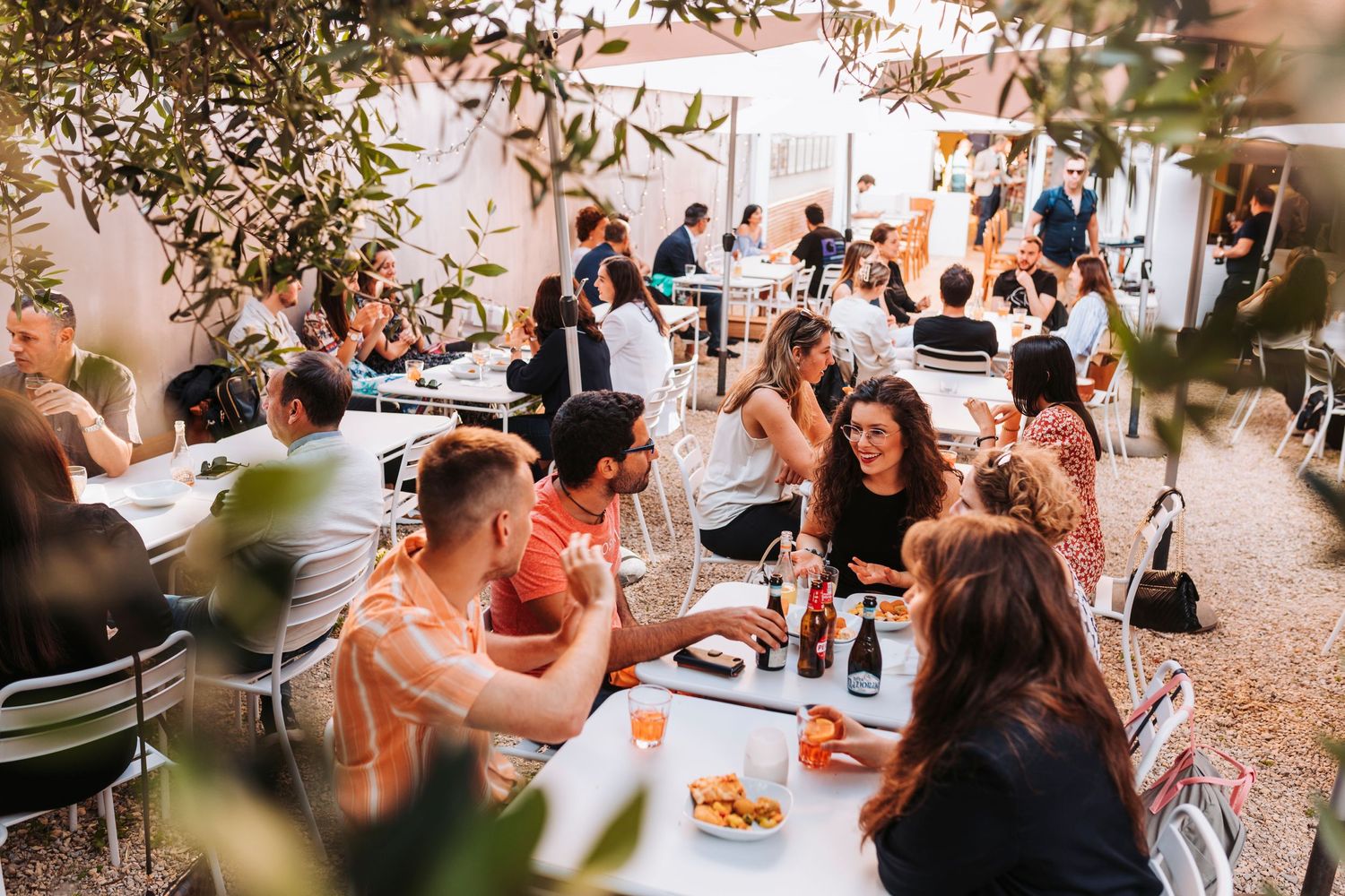 Group of people dining outdoors at casual restaurant with string lights overhead.